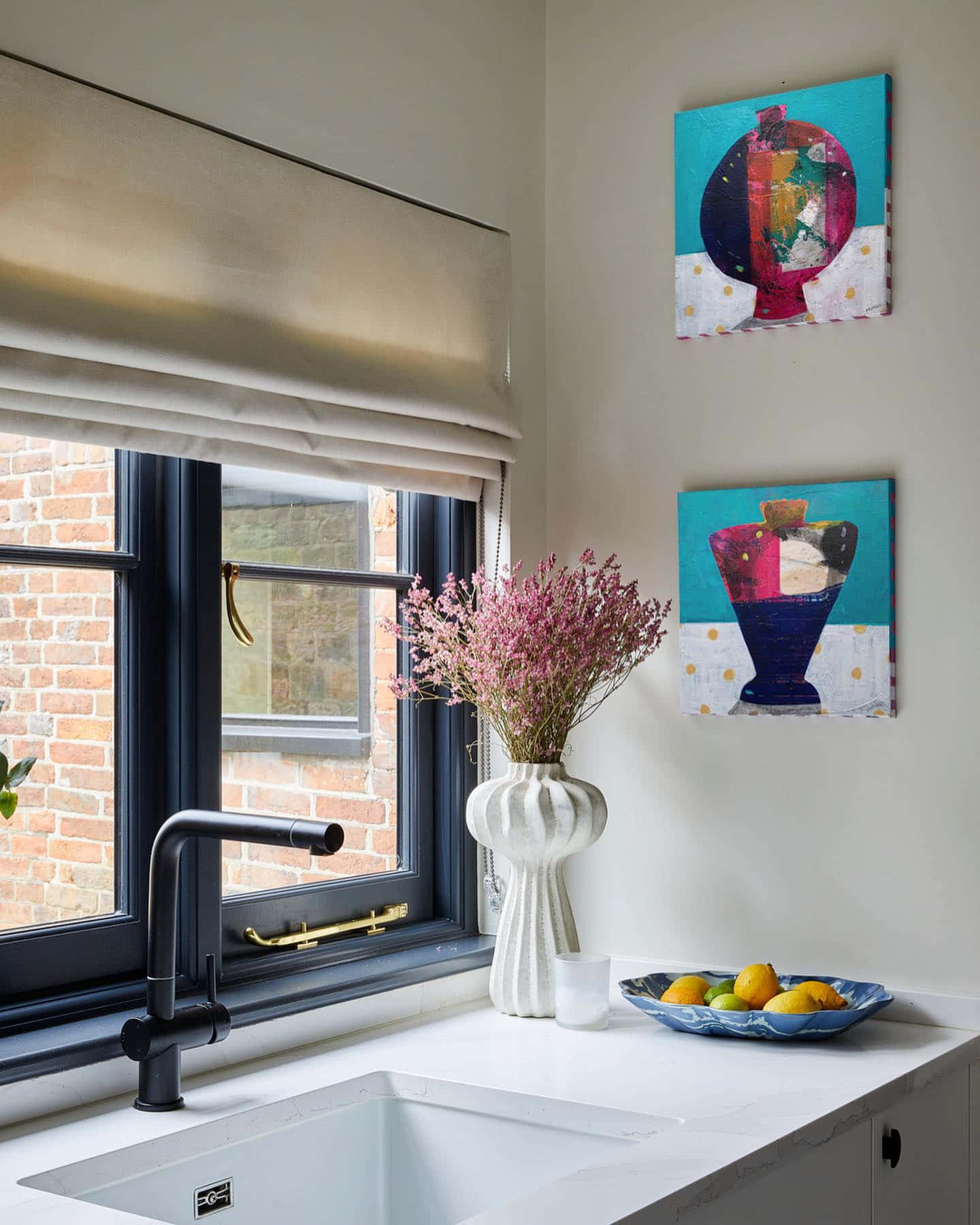 Kitchen Wall 桌布 壁紙 — 現代廚房水槽區域，配有黑色水龍頭、白色檯面，以及白色花瓶中的粉紅色乾花，旁邊是色彩繽紛的抽象藝術品。