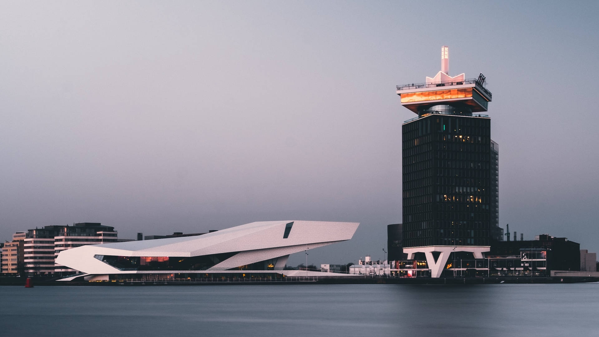 Netherlands 桌布 壁紙 — 現代建築在黃昏時分在平靜的水邊柔和發光，營造出時尚的城市海濱場景。