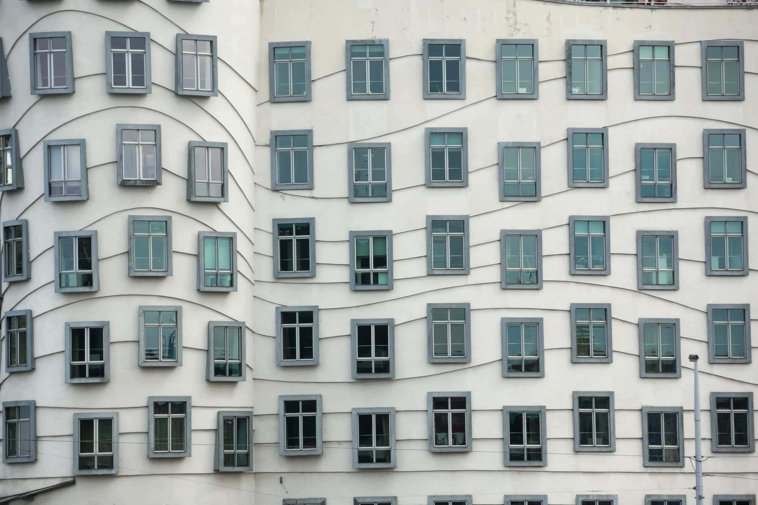 建築 桌布 壁紙 — 現代建築外牆，波浪形白色牆壁和灰色框架窗戶排列成節奏曲線。