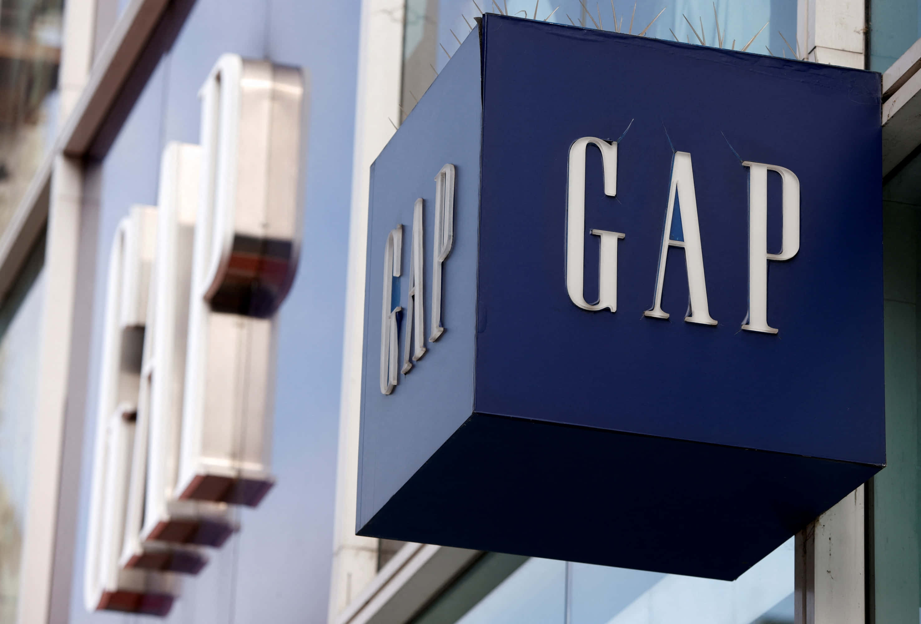 間隙 桌布 壁紙 — 現代建築外牆上安裝的藍色立方體GAP商店招牌特寫，帶有白色字體。