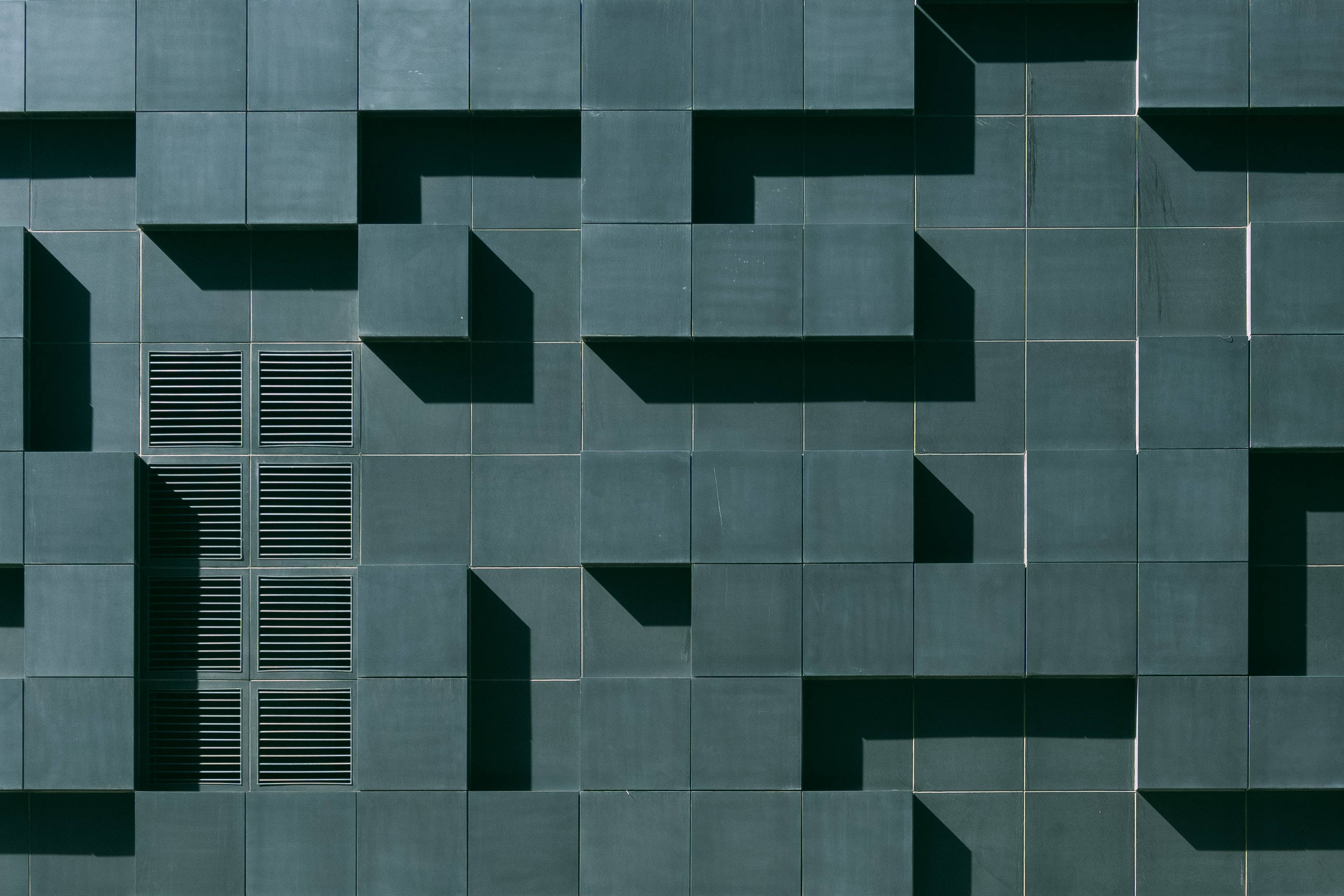 Maze 桌布 壁紙 — 現代建築外牆上的幾何青綠色面板投射出銳利的角狀陰影，形成大膽的抽象圖案。