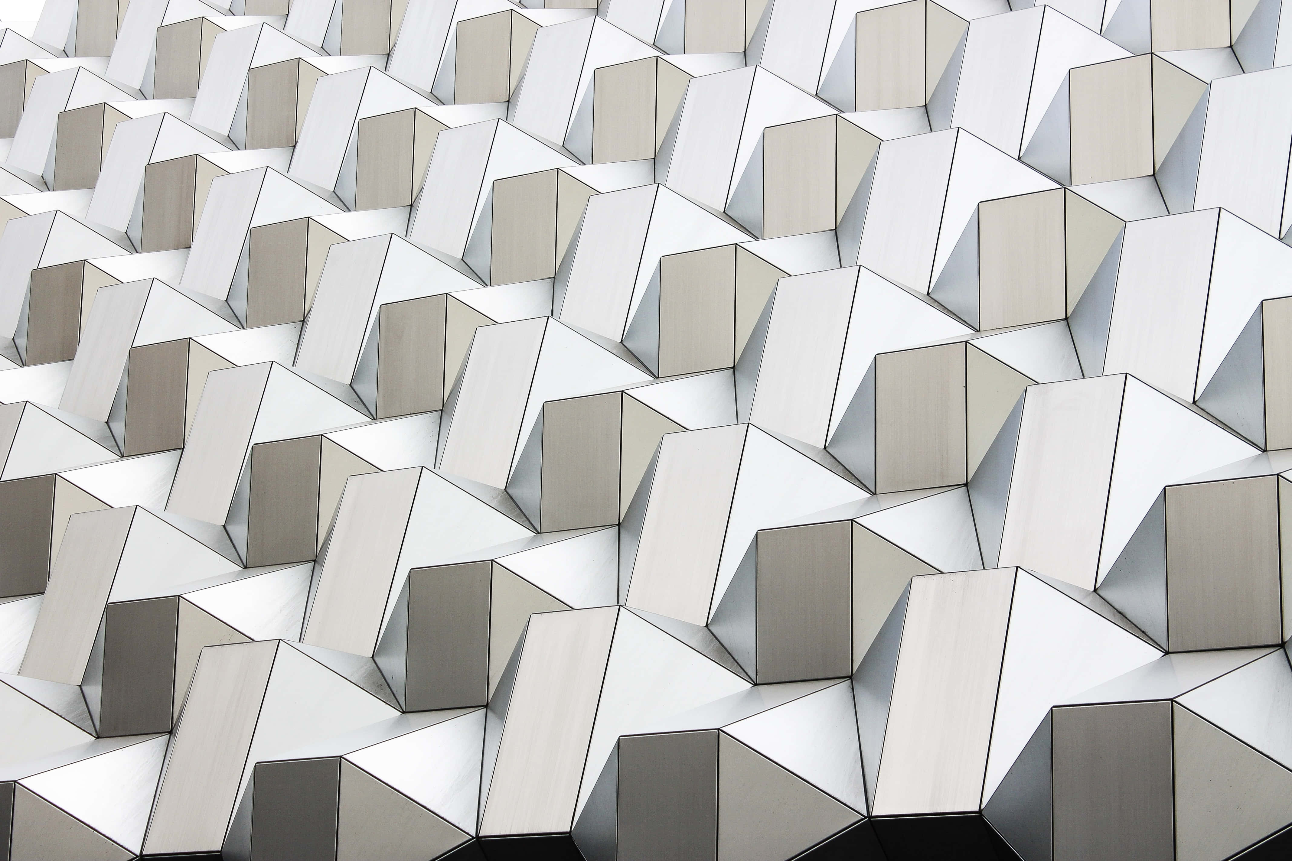 3D 桌布 壁紙 — 現代建築物外牆的特寫，帶有重複的幾何三角形面板，採用銀色和灰色色調。