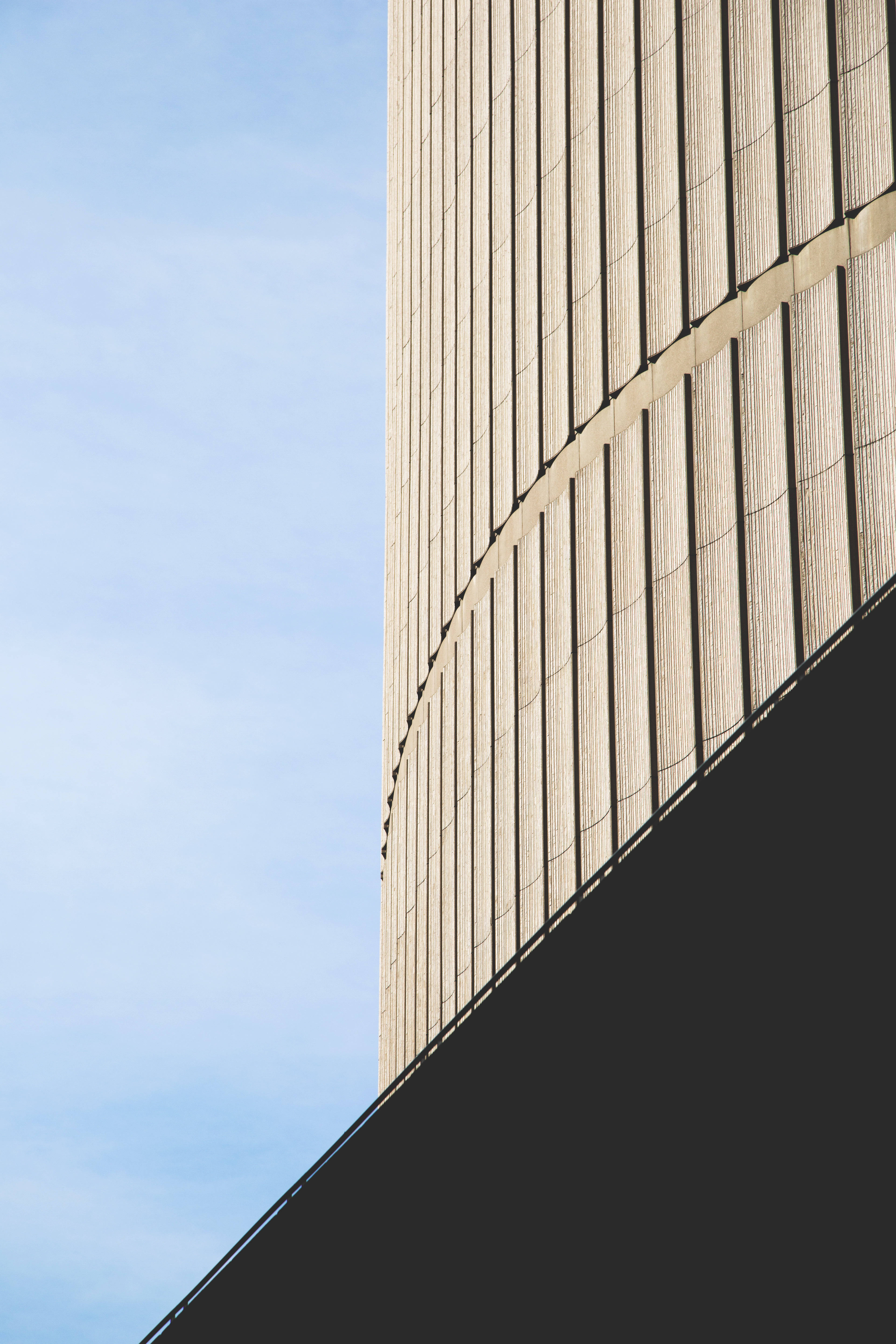 Building 桌布 壁紙 — 現代建築的弧形米色外牆，帶有垂直線條，與清澈的藍天和深色對角陰影形成對比。