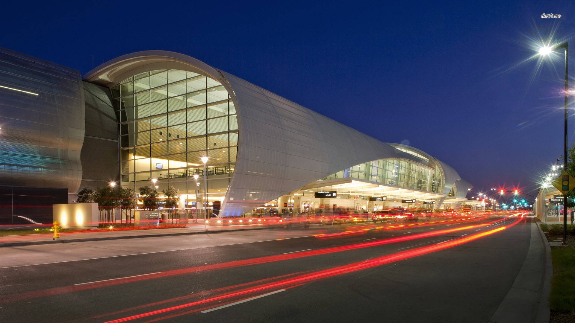 Airport 桌布 壁紙 — 現代彎曲的機場航廈在夜間發光，前景中紅色車燈軌跡模糊成線。