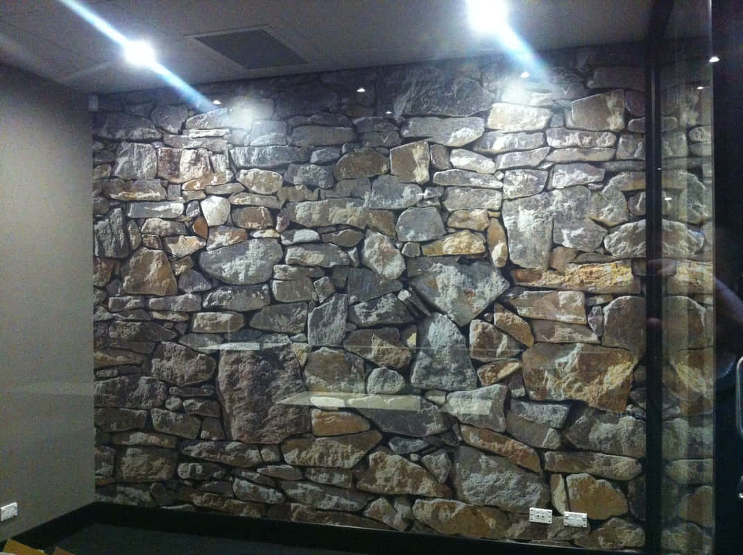 Installation Art 桌布 壁紙 — 現代房間中，在明亮天花板燈光下，帶有各種灰色、棕色和棕褐色石頭的紋理石牆壁紙。