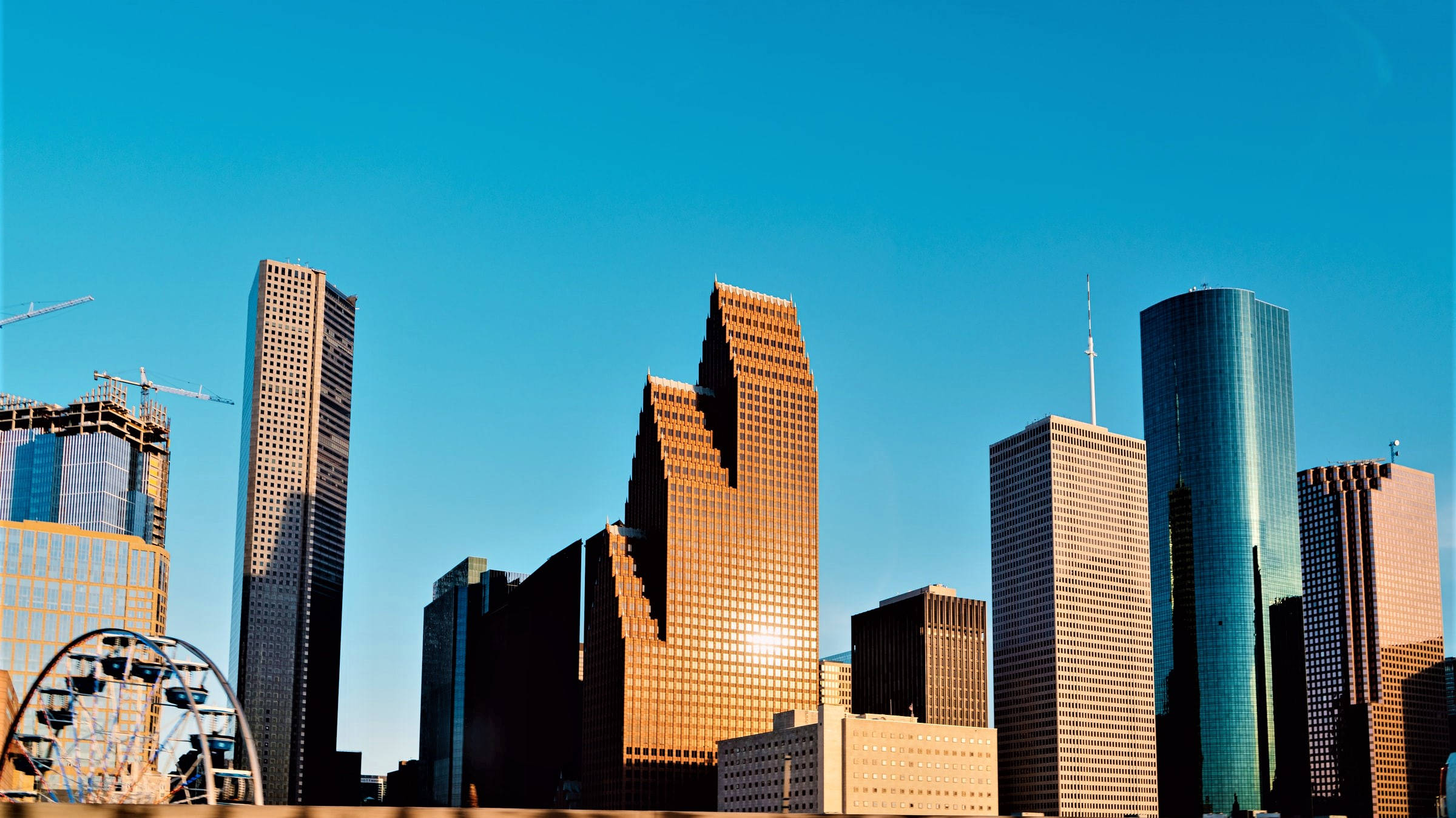 Houston 桌布 壁紙 — 現代摩天大樓以玻璃和鋼鐵外牆聳立在清澈的藍天下，金色的陽光沐浴其表面。
