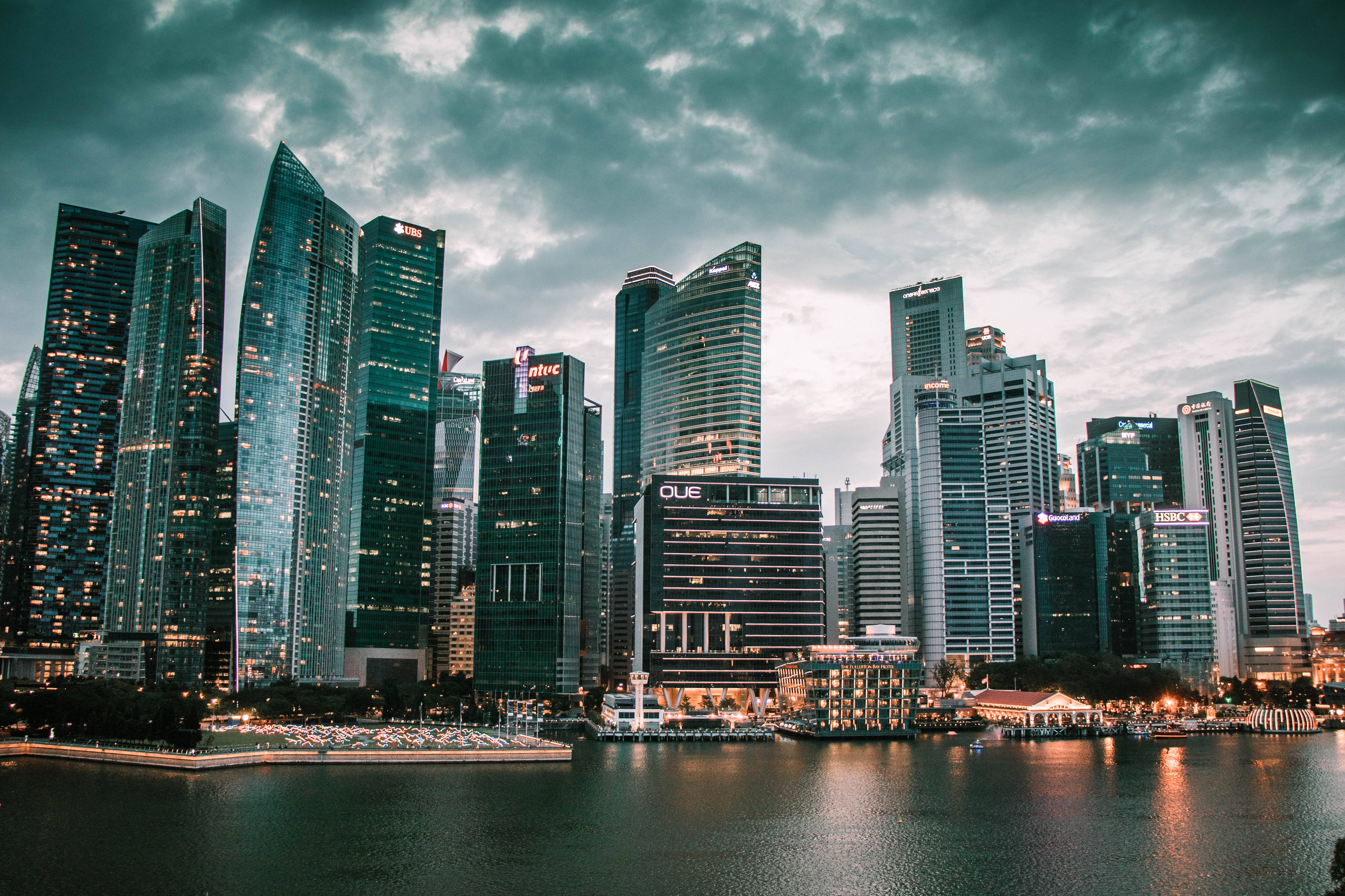 Singapore 桌布 壁紙 — 現代摩天大樓在平靜的水面上倒映，籠罩在憂鬱的暮色雲層下，呈現繁華的城市景觀。