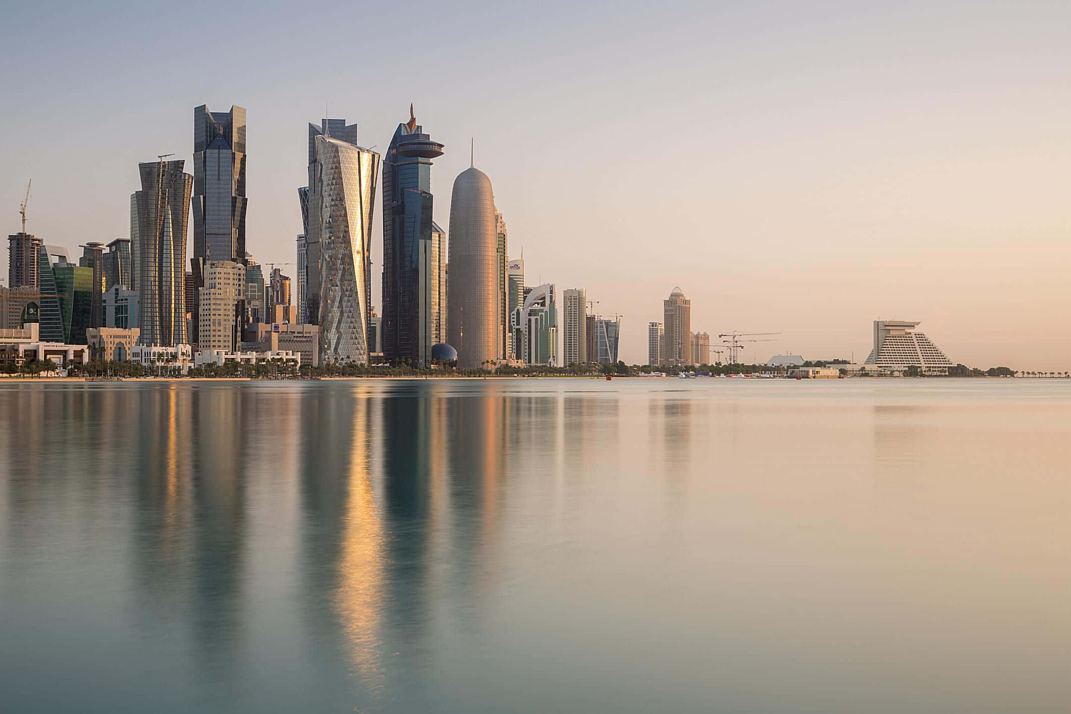 Qatar 桌布 壁紙 — 現代摩天大樓的反射玻璃外牆在金色日落時分倒映在平靜的水面上。