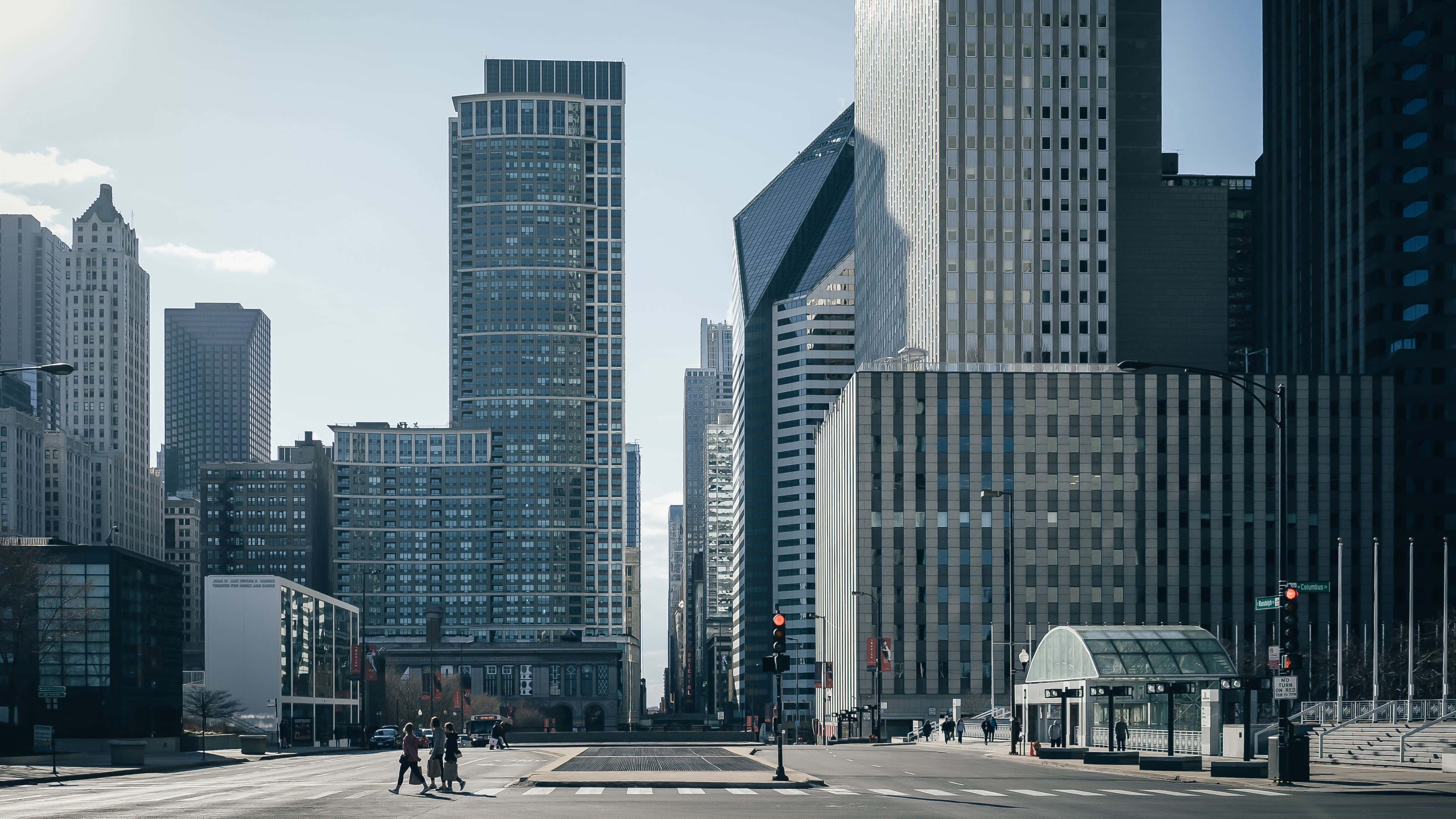 4K Ultra HD Chicago 桌布 壁紙 — 現代摩天大樓聳立在寬闊的城市街道上，行人正在晴朗的藍天下過馬路。