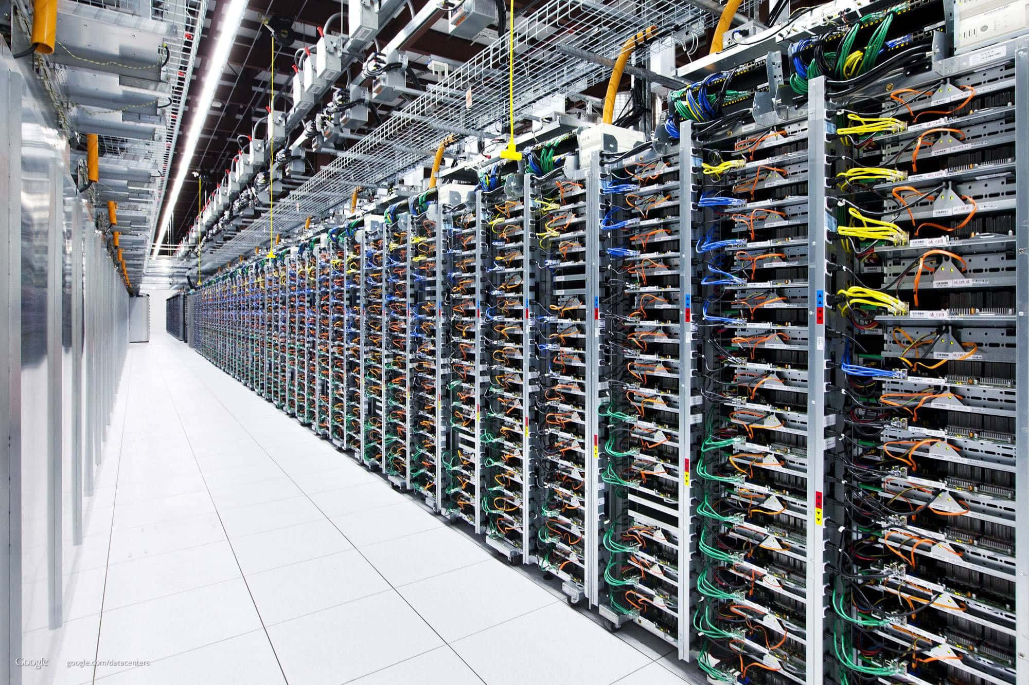 data 桌布 壁紙 — 現代數據中心中一條長長的伺服器機架走廊，充滿了彩色電纜和閃爍的燈光。