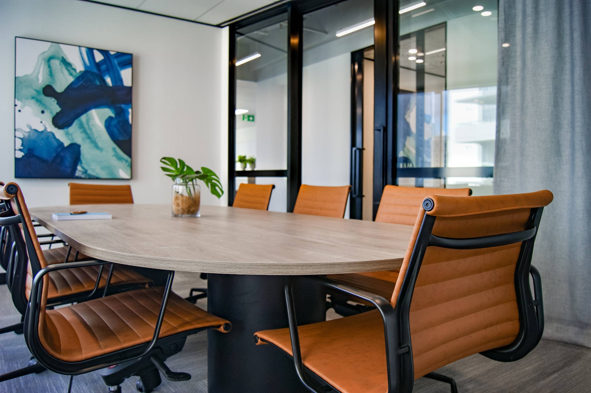 Office Space 桌布 壁紙 — 現代會議室，配有木桌、橙色椅子、玻璃牆和白色牆上的抽象藍色藝術品。