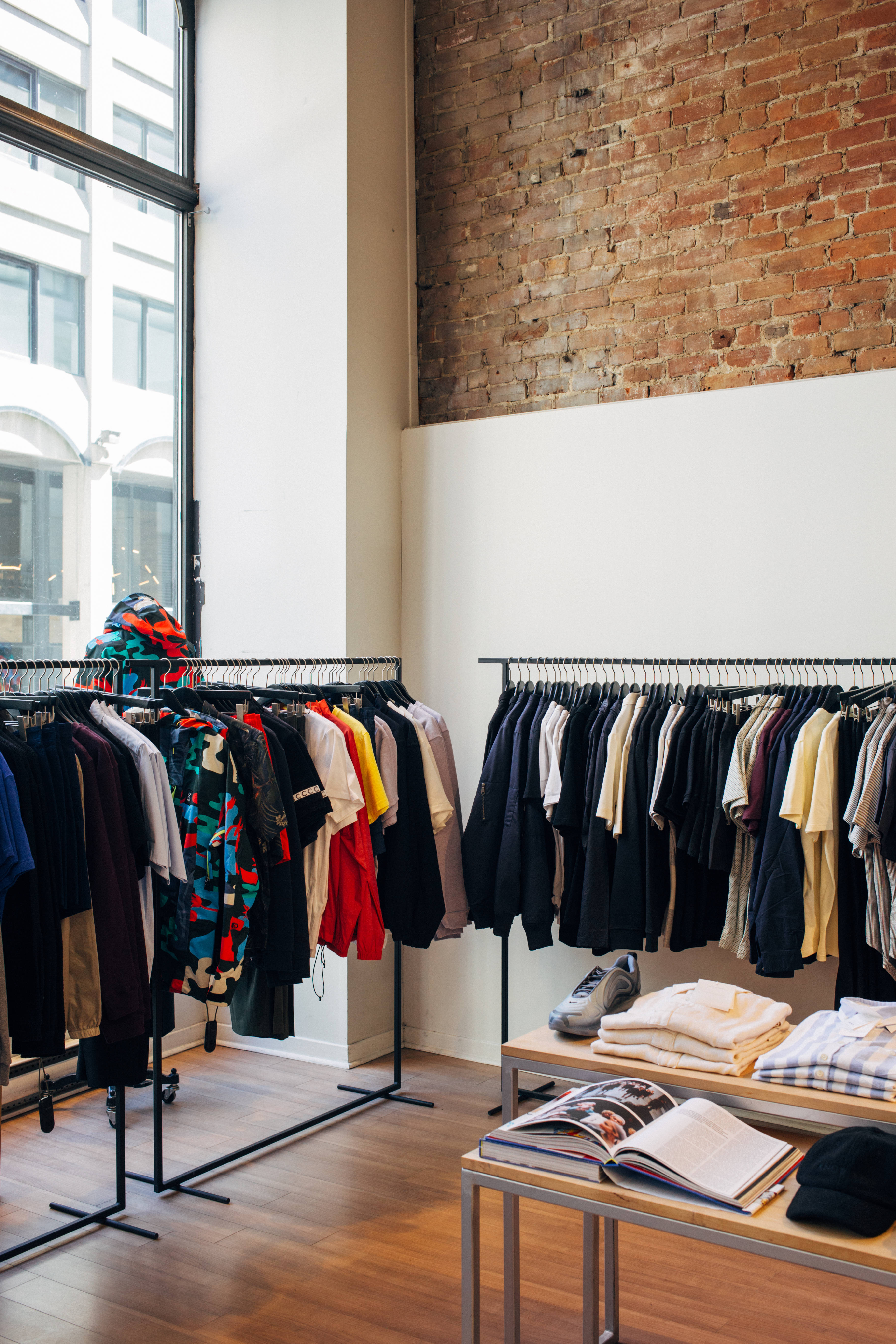Trendy 桌布 壁紙 — 現代服裝店，陳列著色彩繽紛的衣物，背景是裸露的磚牆和大窗戶。