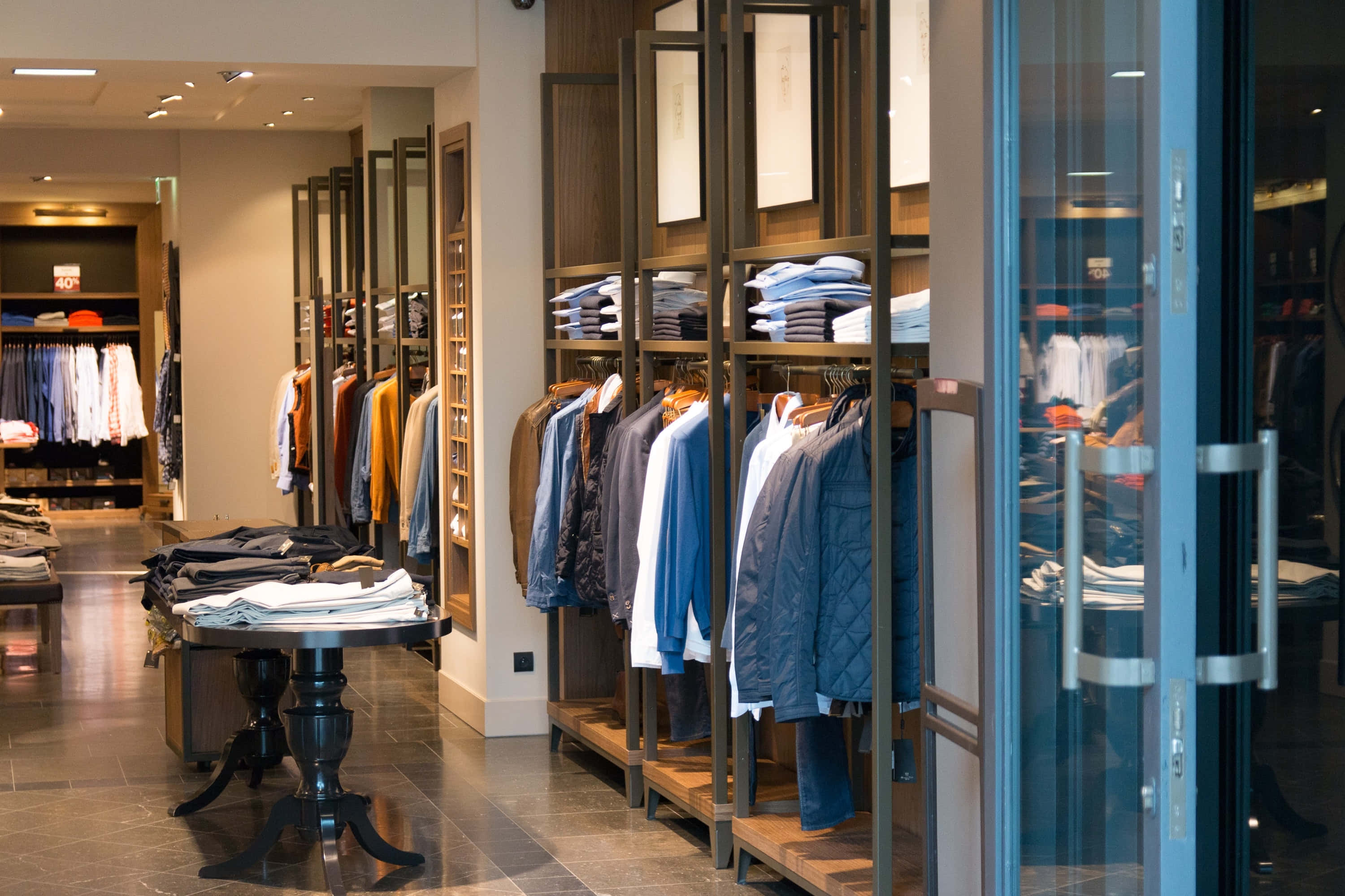 Clothes 桌布 壁紙 — 現代服裝店內部，明亮的頂燈下整齊排列著襯衫、夾克和折疊衣物的貨架。