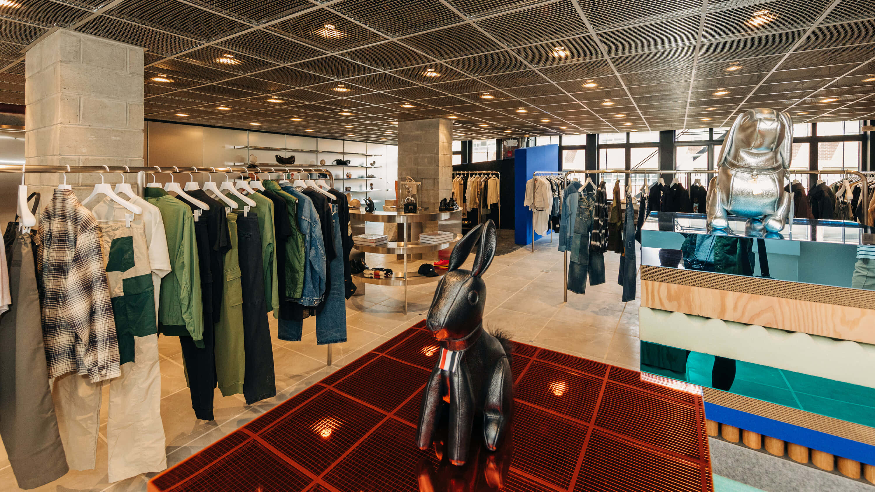 潮流玩家 桌布 壁紙 — 現代服裝店內部，設有服裝架和色彩繽紛的平台上引人注目的黑色和銀色兔子雕塑。