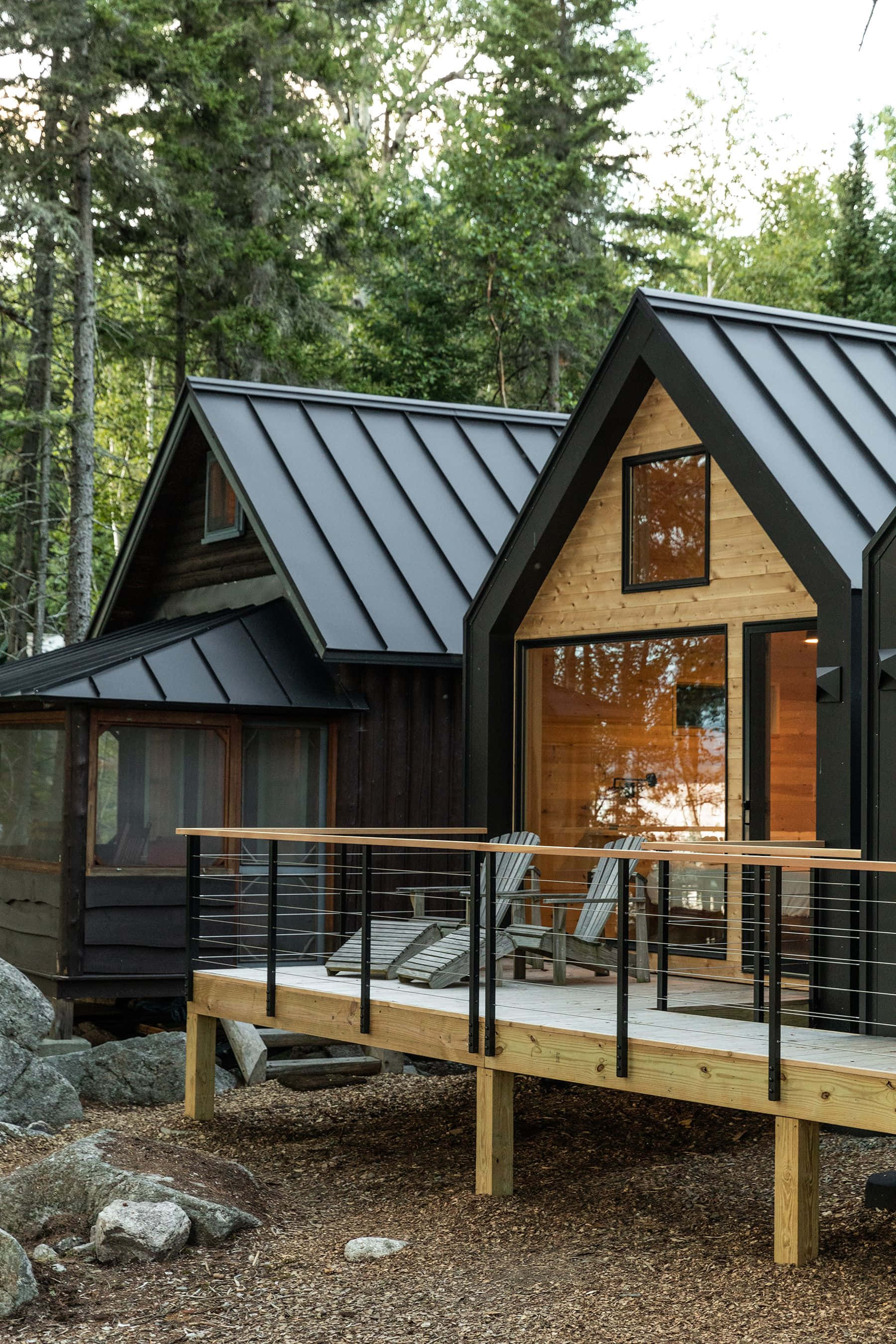 cabin 桌布 壁紙 — 現代木屋，黑色金屬屋頂，坐落在森林山坡上，周圍是高聳的松樹。