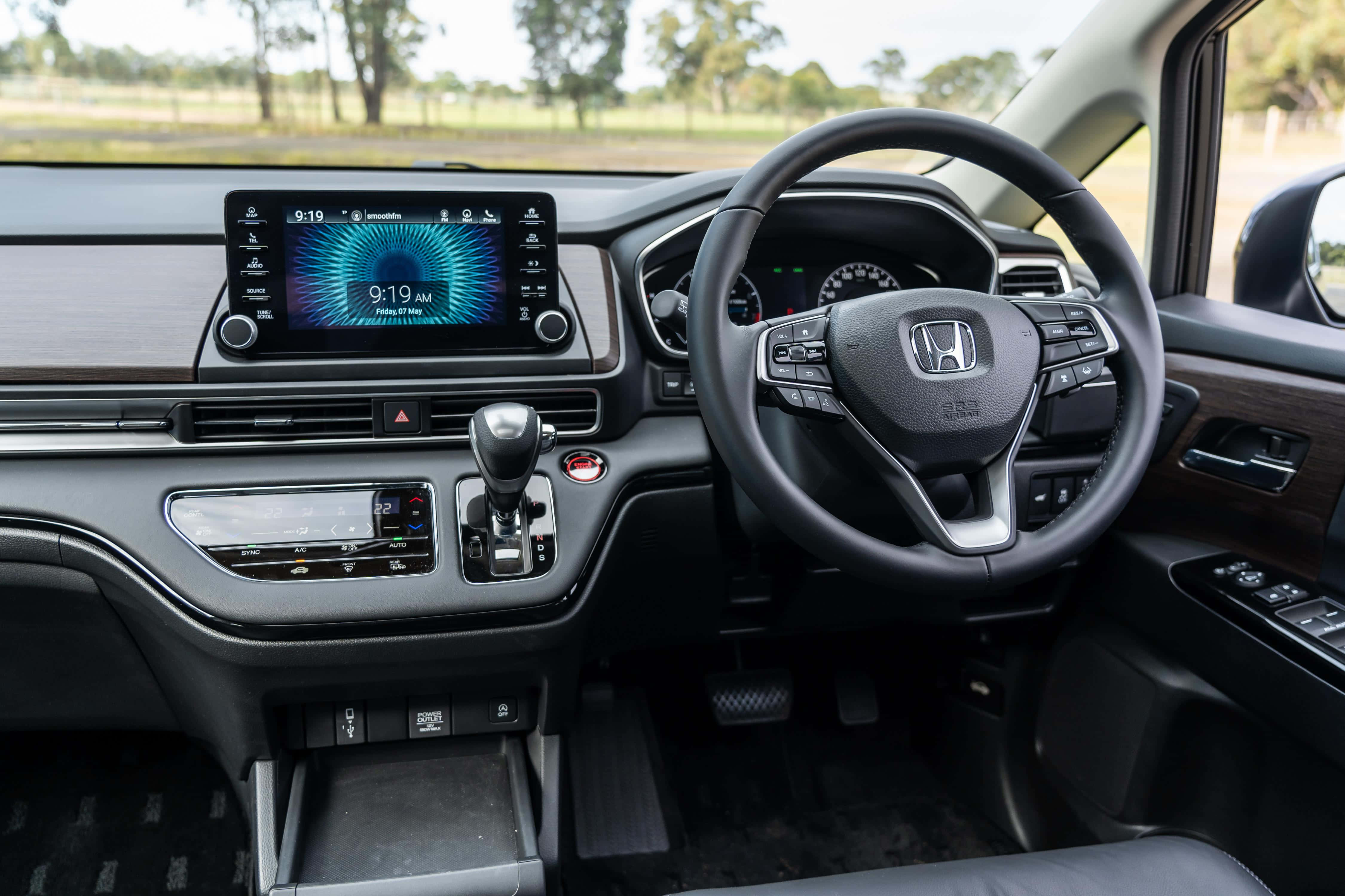 Honda Odyssey 桌布 壁紙 — 現代本田汽車內裝，配備數位儀表板和方向盤，顯示上午9:19，背景為模糊的綠色田野。