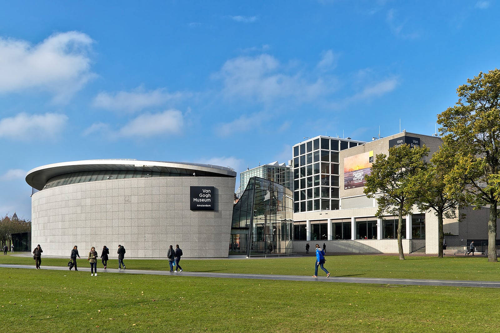 Museum 桌布 壁紙 — 現代梵谷博物館建築，擁有彎曲石頭外牆和玻璃翼，在明亮的藍天和散落的雲朵下。