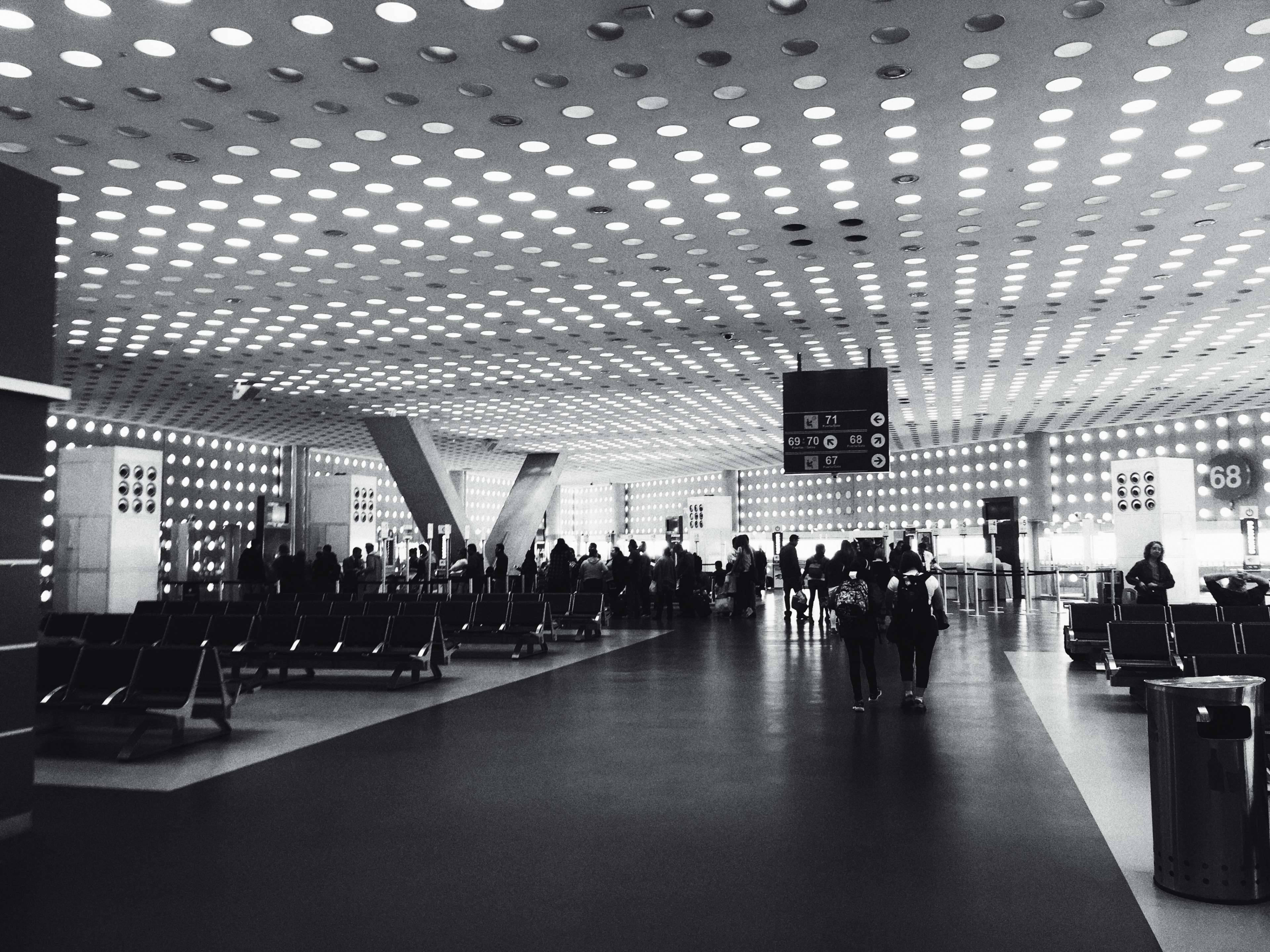 Airport 桌布 壁紙 — 現代機場航廈的黑白照片，帶有圖案天花板燈和旅客走過一排排座位。