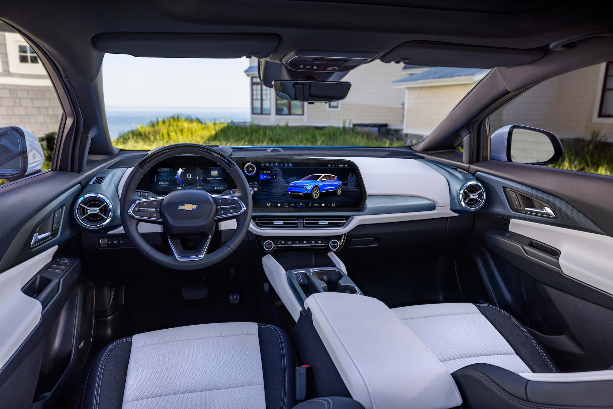 Chevrolet 桌布 壁紙 — 現代汽車內裝，配備白色皮革座椅和數位儀表板，俯瞰沿海住宅和海洋。