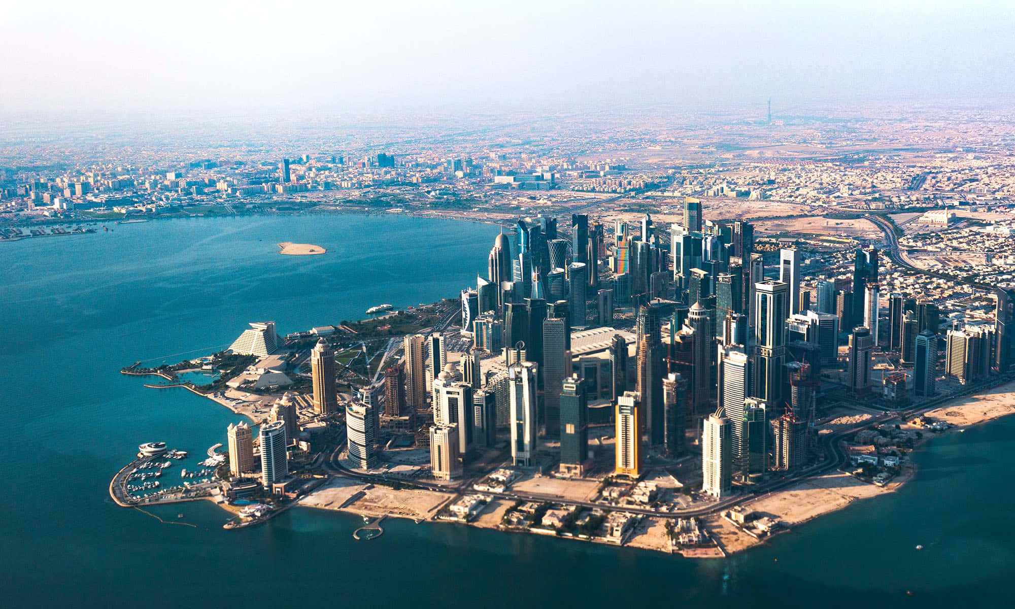 Qatar 桌布 壁紙 — 現代沿海城市景觀的鳥瞰圖，高聳的摩天大樓和圍繞半島的碧綠海水。