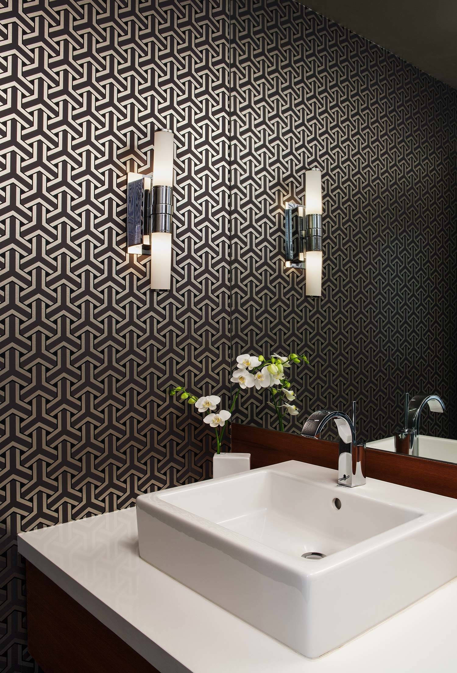 Interior Design 桌布 壁紙 — 現代浴室，白色洗手盆置於木製洗手台上，背景為深色幾何圖案壁紙，搭配時尚壁燈和白色蘭花。
