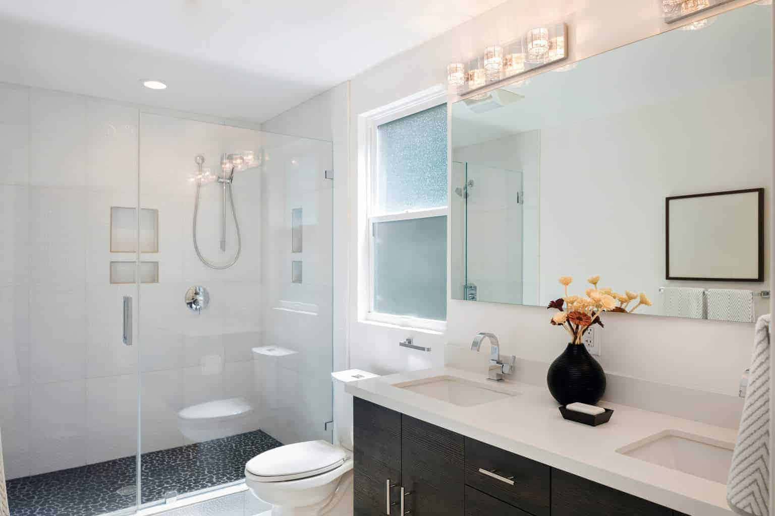 Bathroom Decor 桌布 壁紙 — 現代浴室，配有白色瓷磚、玻璃淋浴間、深色木製洗手台和黑色花瓶中的黃色花朵。