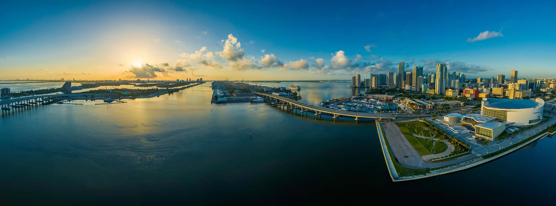 城市 桌布 壁紙 — 現代海岸城市的全景日落景觀，橋樑、水域和摩天大樓在充滿活力的藍天下。
