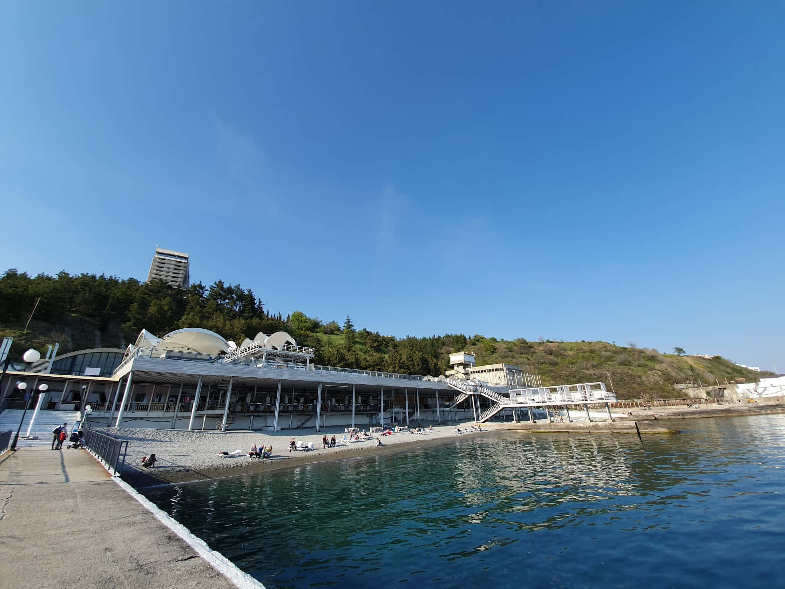 Ocean Beach 桌布 壁紙 — 現代海邊亭閣，帶有弧形白色屋頂，俯瞰晴朗天空下平靜的藍色海水。