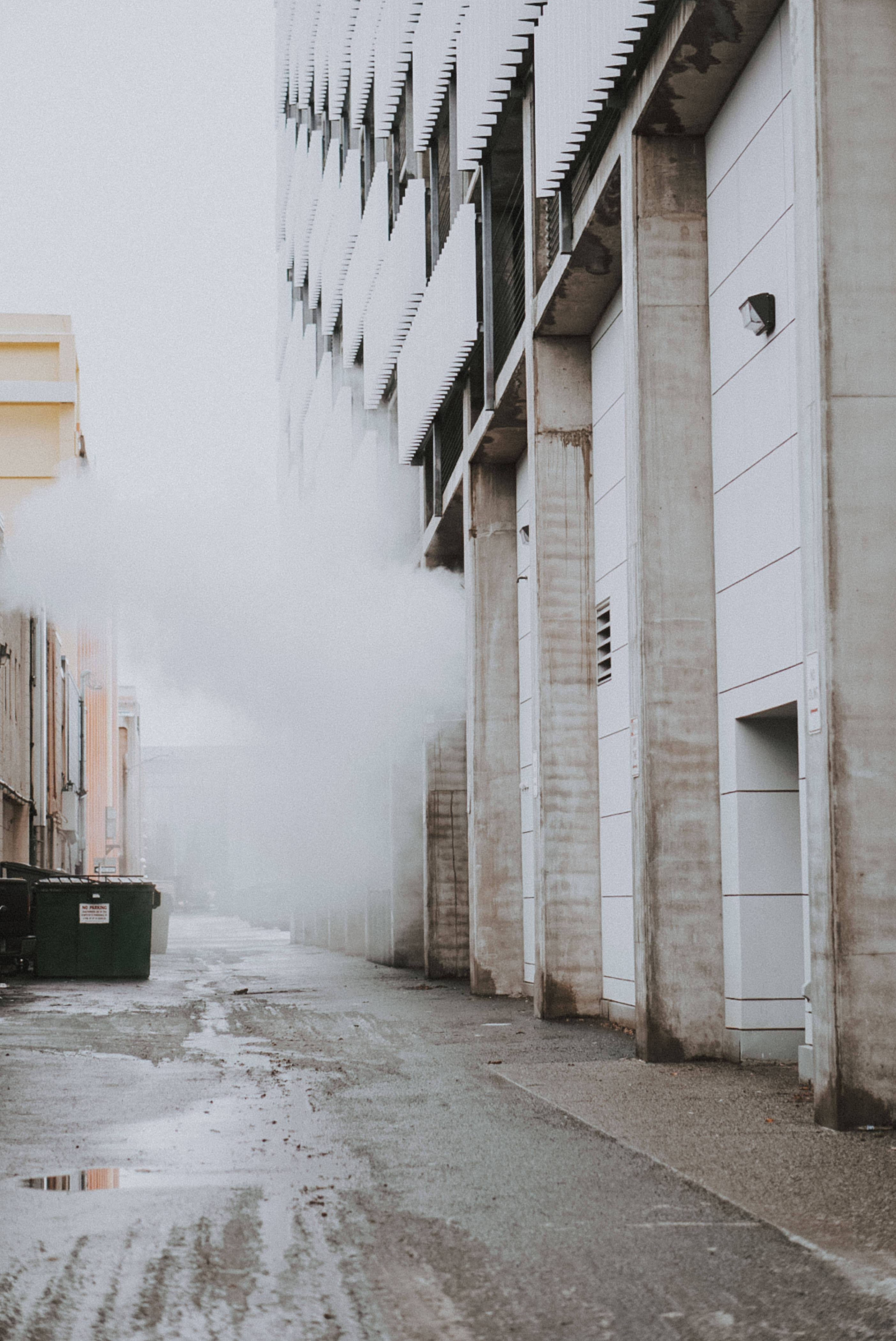 Street 桌布 壁紙 — 現代混凝土建築物之間一條霧氣瀰漫的都市小巷，濕漉漉的路面反射著陰天。