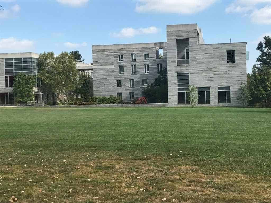  壁紙 — 現代混凝土建築物搭配玻璃窗，矗立於廣闊綠色草坪後方，上方是帶有零星白雲的明亮藍天。