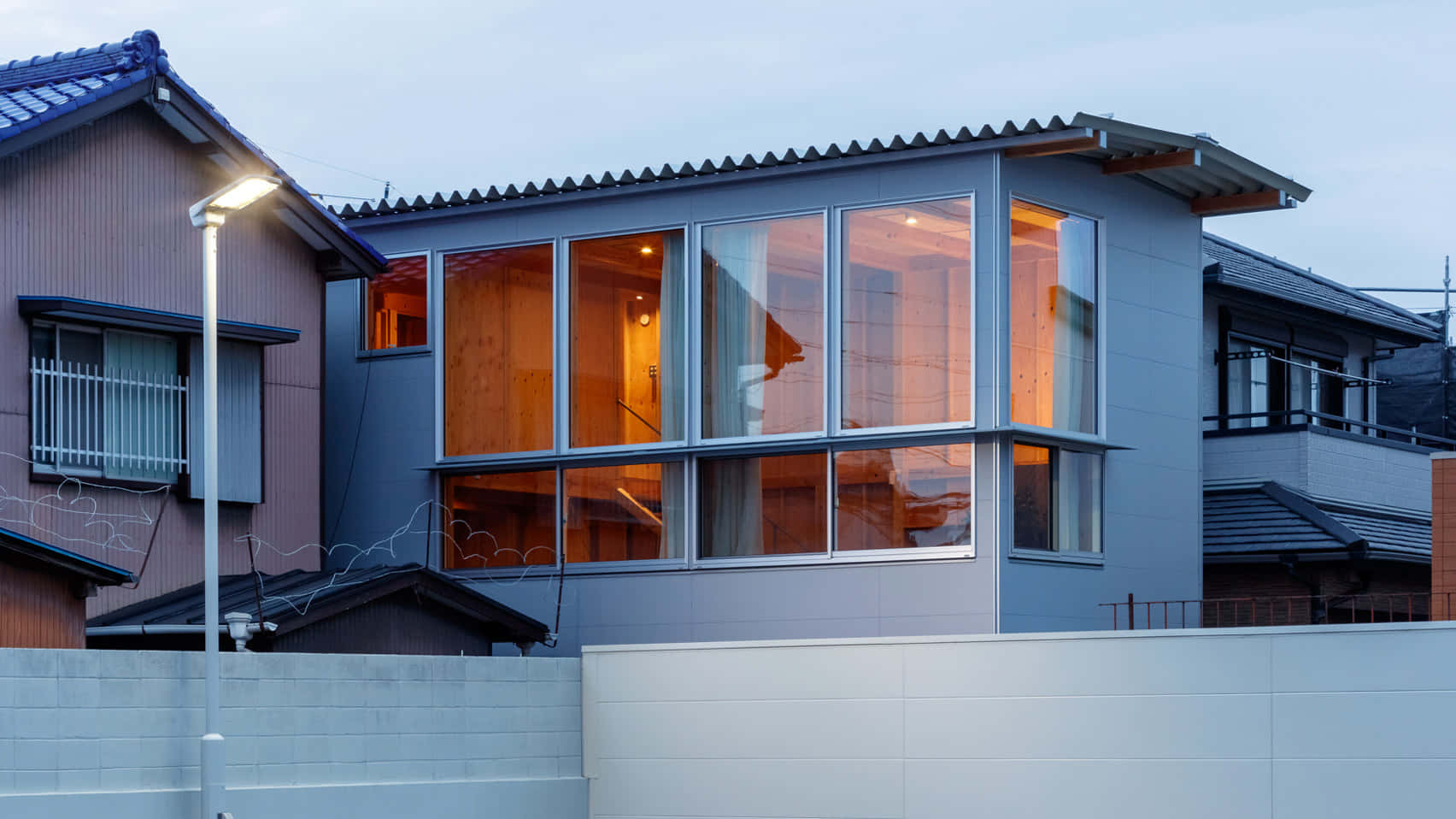 Minimalist Architecture 桌布 壁紙 — 現代灰色房屋，配備大型玻璃窗，在暮色天空中散發溫暖光芒。