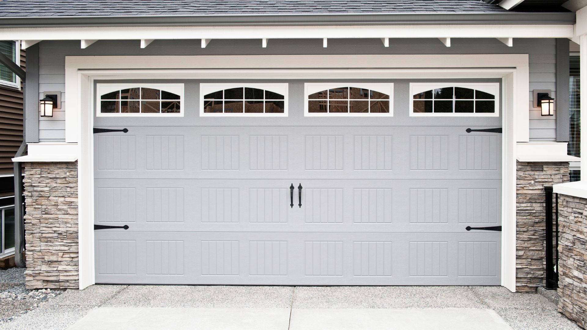 Garage 桌布 壁紙 — 現代灰色車庫門，帶拱形窗戶和黑色五金件，安裝在帶有石柱和白色飾邊的房子上。