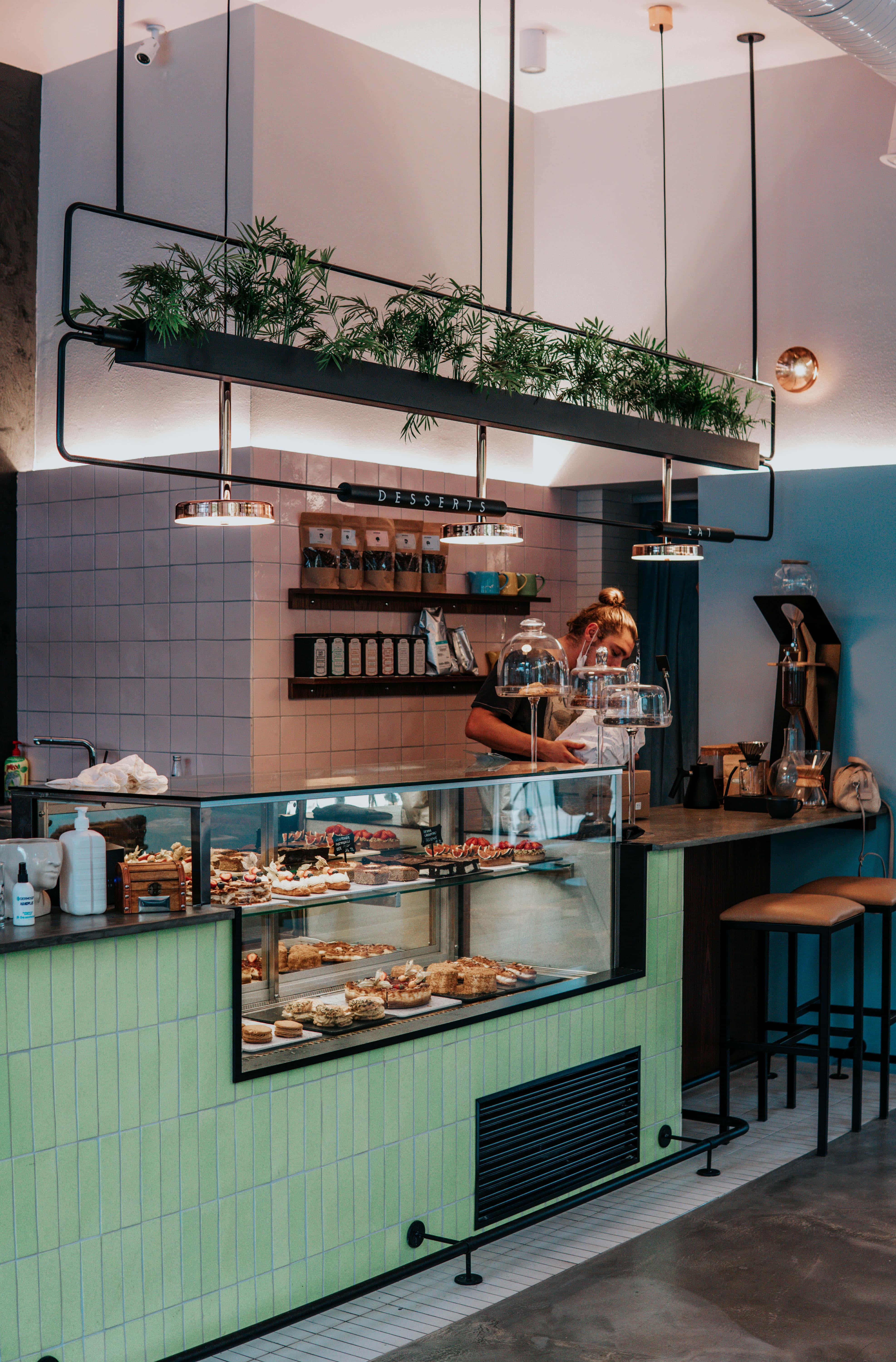 Barista 桌布 壁紙 — 現代烘焙店內部，薄荷綠色磁磚檯面展示玻璃下的糕點，員工在檯後工作。