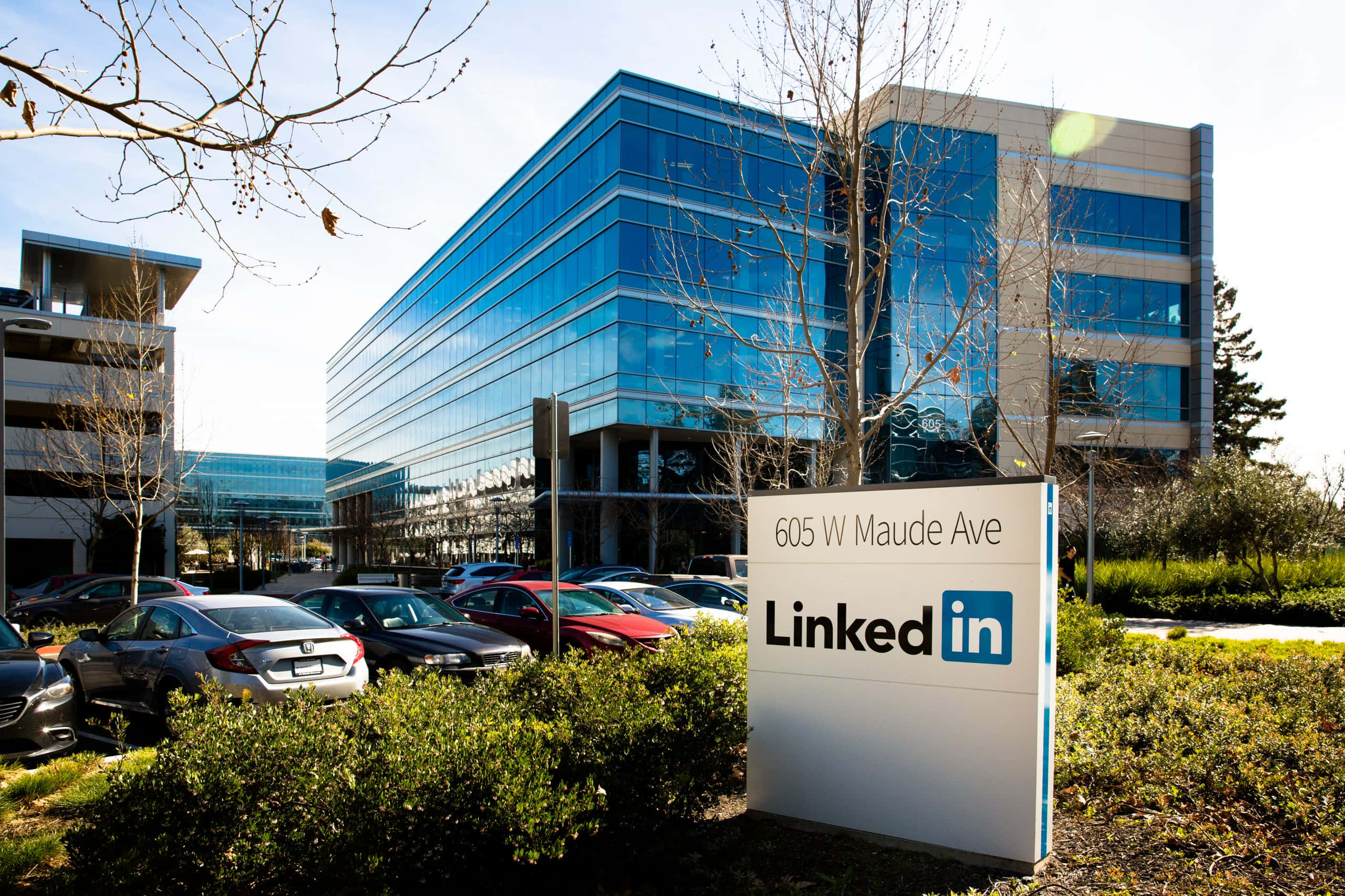 Linkedin 桌布 壁紙 — 現代玻璃LinkedIn辦公大樓，設有顯眼標誌和停車場，在晴朗藍天下。