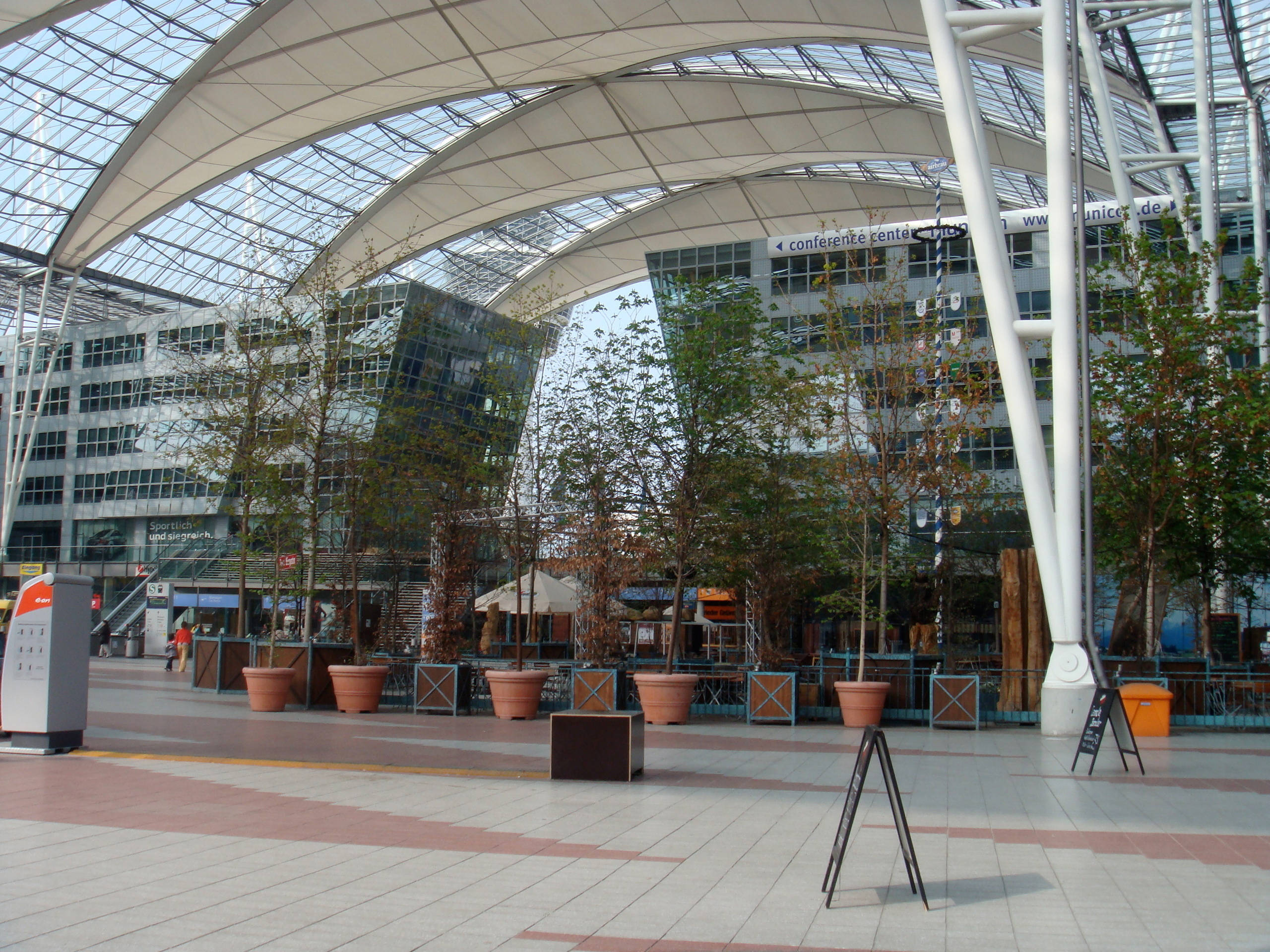 Airport 桌布 壁紙 — 現代玻璃及鋼結構中庭，設有盆栽樹木及瓷磚地板，上方為弧形屋頂。