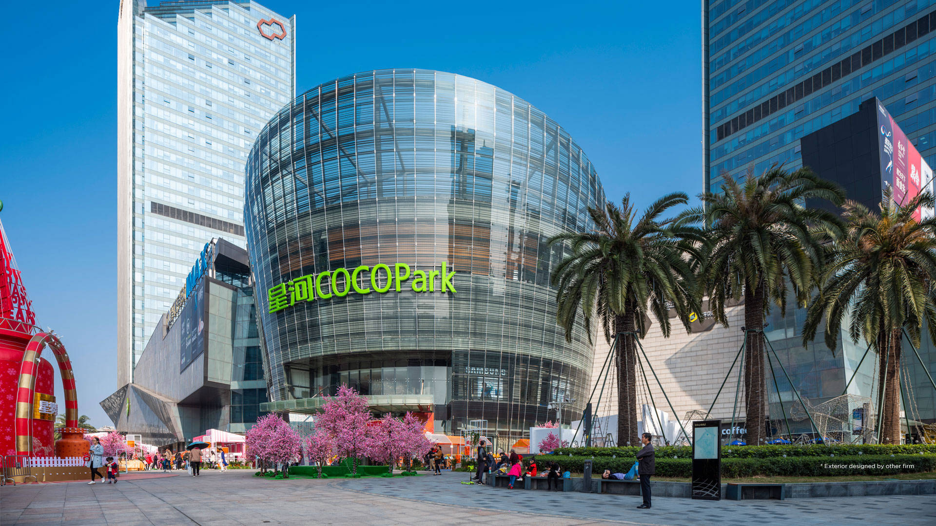 Shenzhen 桌布 壁紙 — 現代玻璃圓頂COCO Park購物中心在晴朗藍天下閃耀，前景有粉紅櫻花和棕櫚樹。