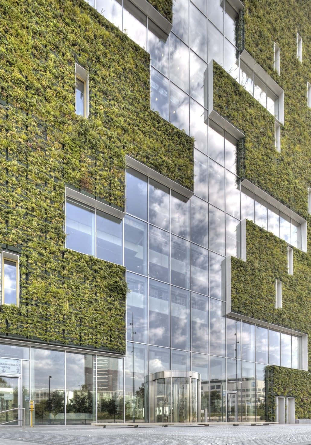 Green Buildings 桌布 壁紙 — 現代玻璃建築外牆，擁有茂密的綠色垂直花園，映照著多雲的天空。