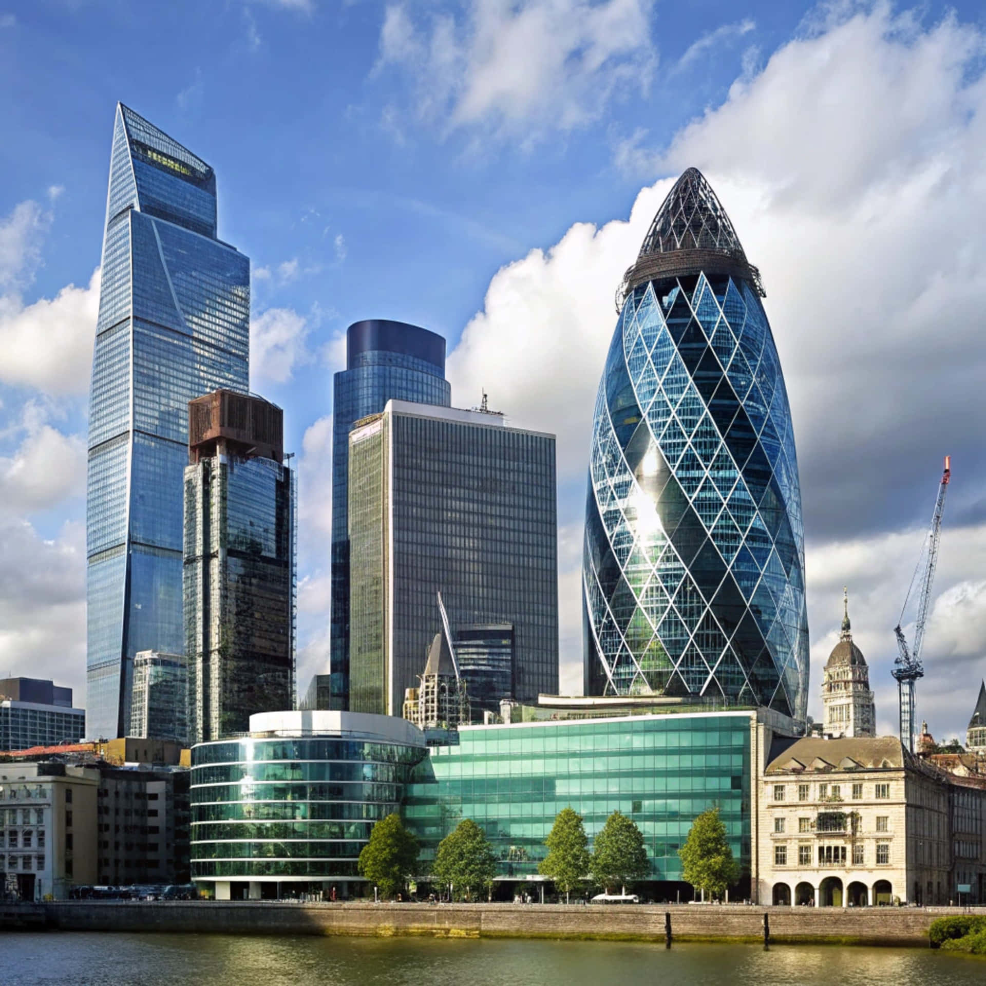 London Skyline 壁紙 — 現代玻璃摩天大樓，包括小黃瓜大廈，在河邊的藍天白雲下聳立。