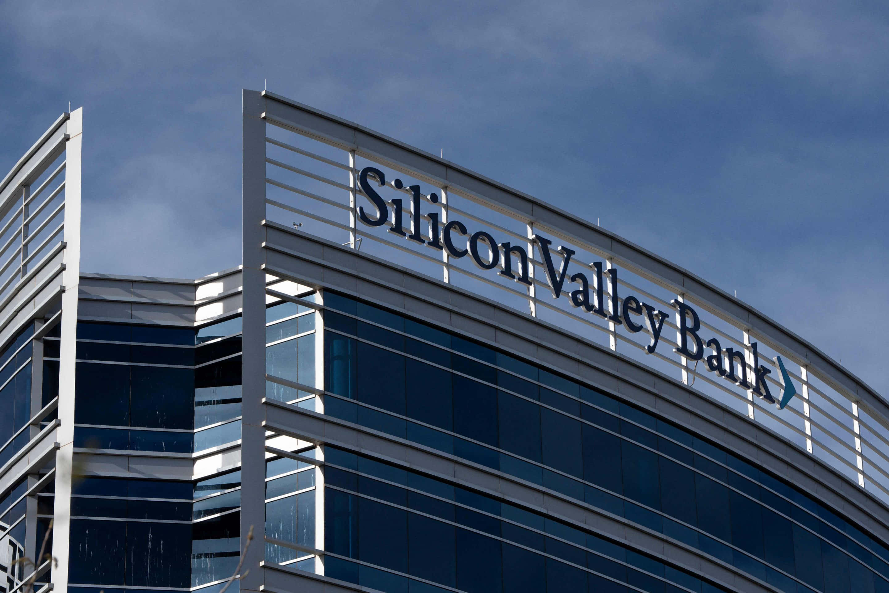 Bank 桌布 壁紙 — 現代玻璃摩天大樓，帶有「Silicon Valley Bank」標誌，背景為多雲的藍天。
