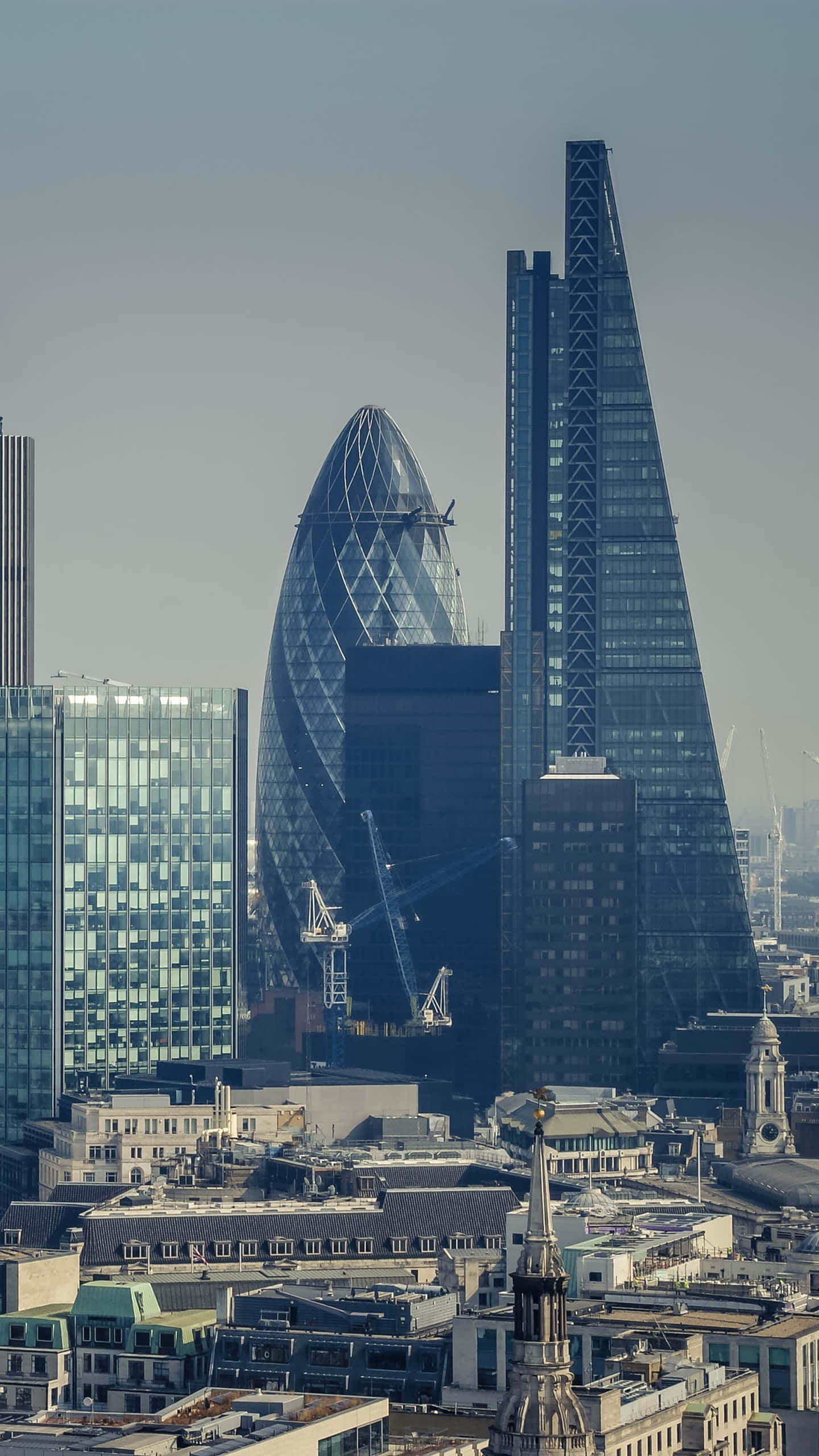 Skyscraper 桌布 壁紙 — 現代玻璃摩天大樓刺穿霧濛濛的天空，下方是密集的城市景觀和歷史屋頂。