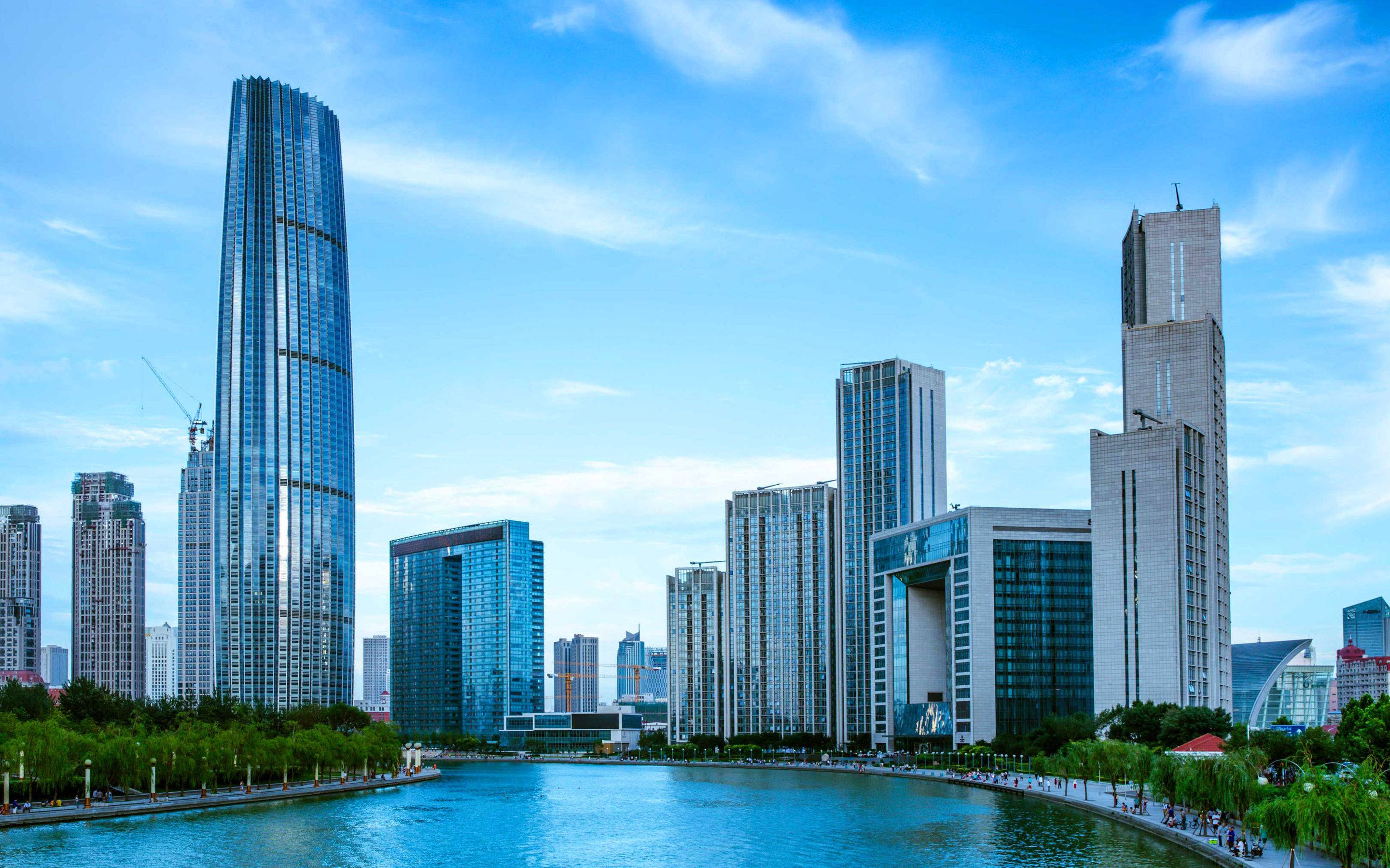 Tianjin 桌布 壁紙 — 現代玻璃摩天大樓在充滿活力的城市海濱場景中反射藍天和碧水。
