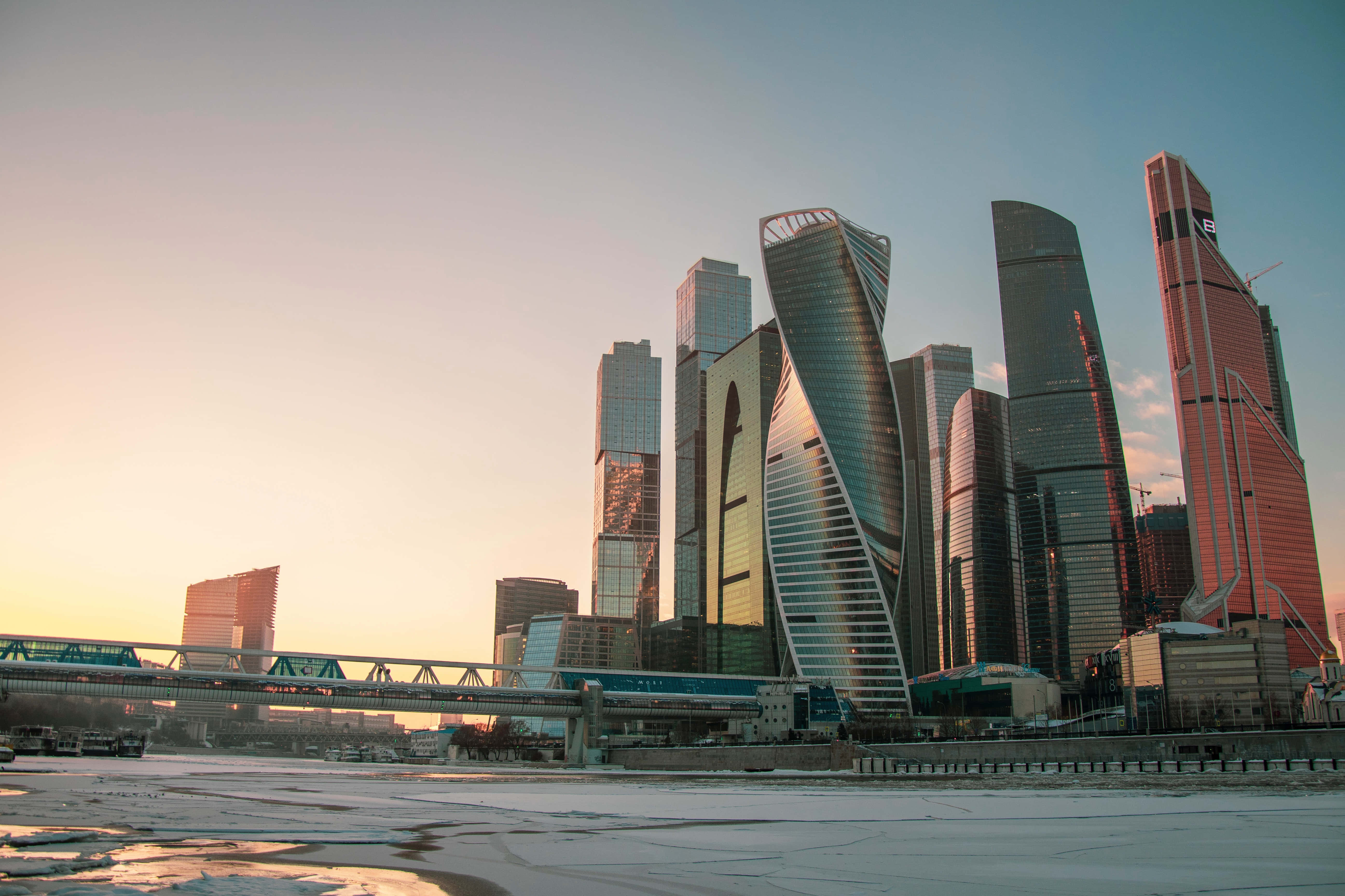 Russian 桌布 壁紙 — 現代玻璃摩天大樓在冬日城市景觀中，將金色日落光線反射在結冰的河流上。