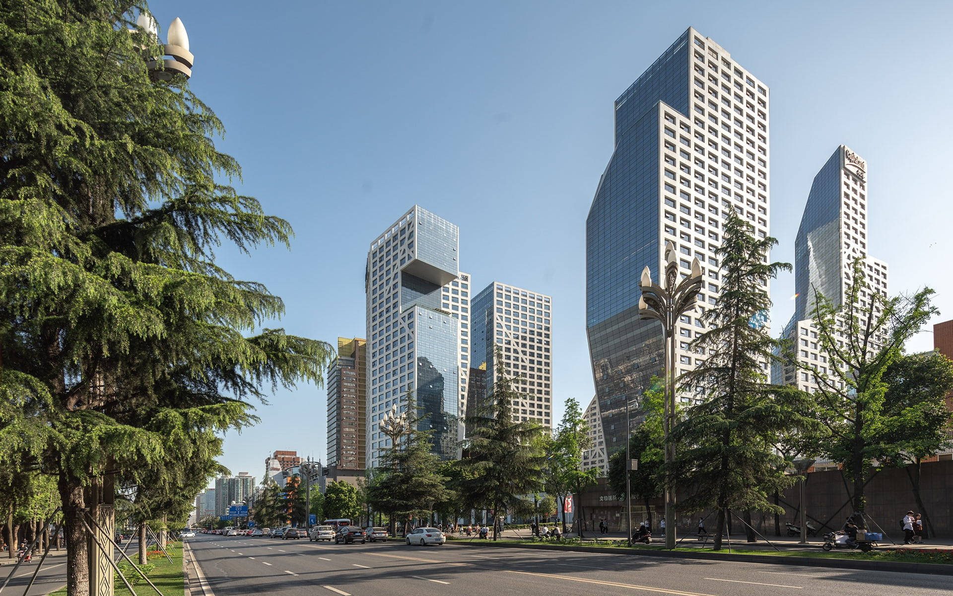 Chengdu 桌布 壁紙 — 現代玻璃摩天大樓在晴朗的藍天下聳立，兩旁是茂密的綠樹，排列在城市街道上。
