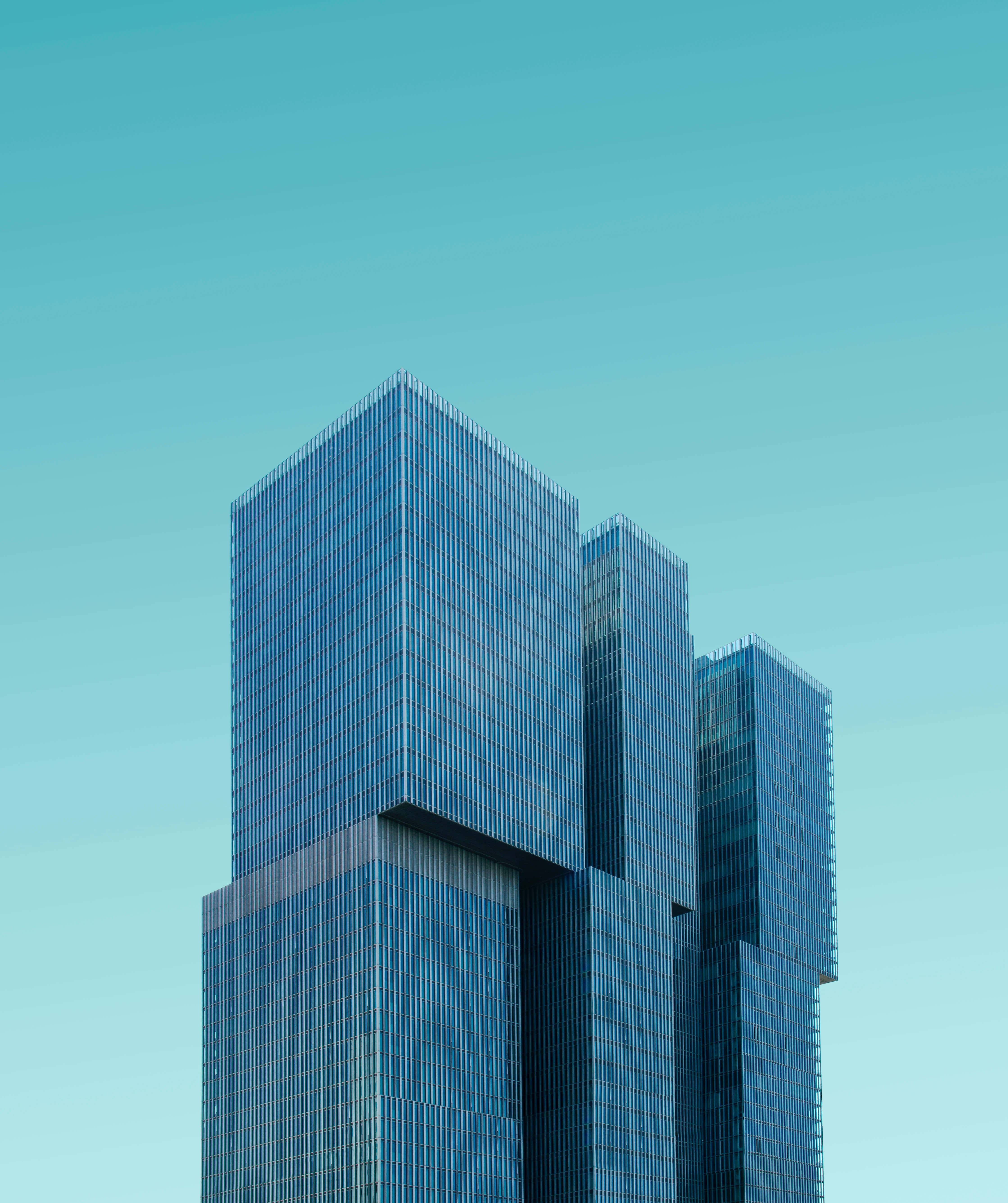 Building 桌布 壁紙 — 現代玻璃摩天大樓在晴朗的藍綠色天空下聳立，形成極簡的城市天際線。