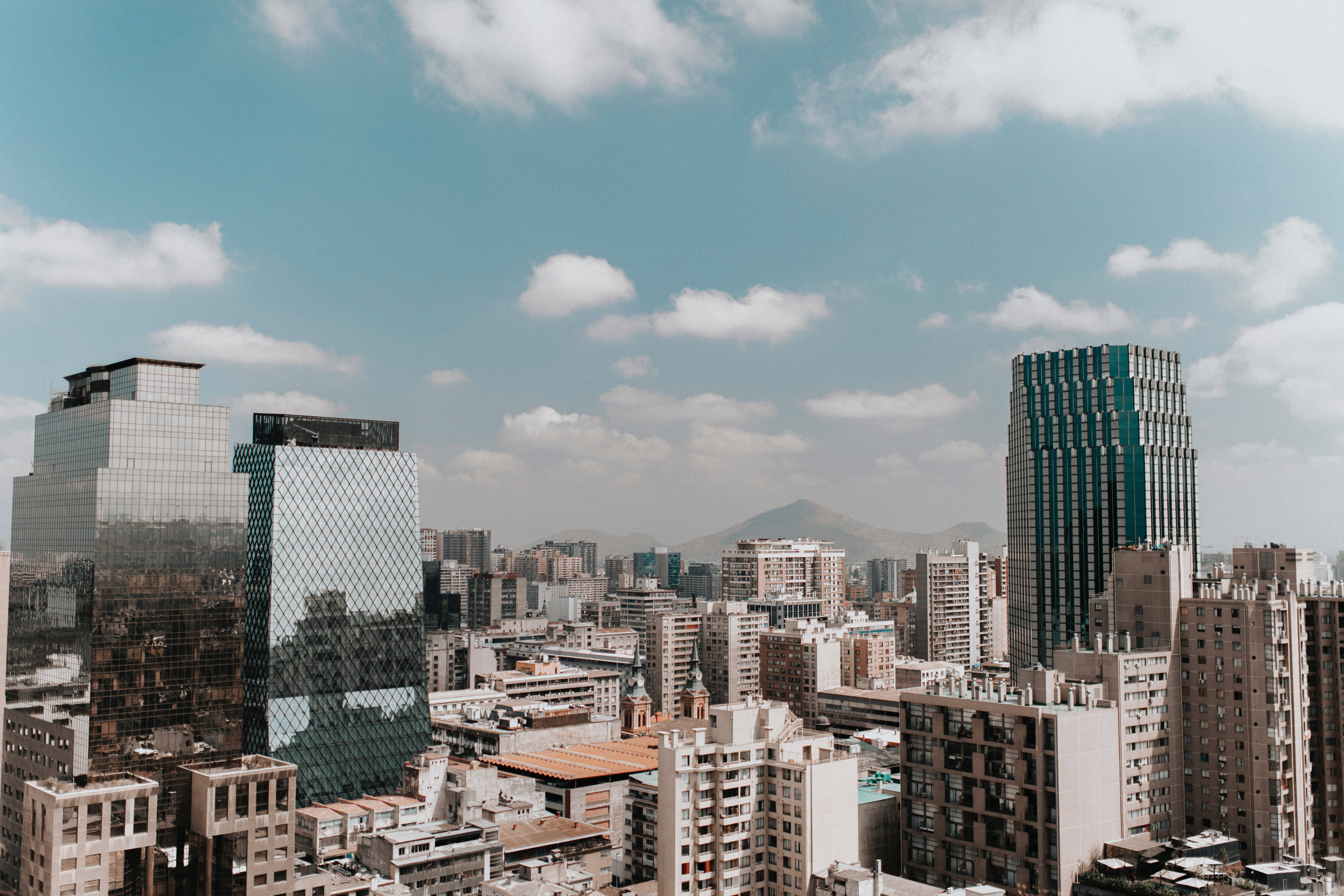 Buildings 桌布 壁紙 — 現代玻璃摩天大樓在晴朗藍天和 fluffy 白雲下，聳立於密集的城市擴展區之上。