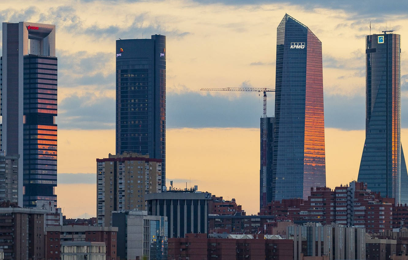 Madrid 桌布 壁紙 — 現代玻璃摩天大樓在繁忙的城市天際線中，映照著多雲天空下的金色日落色調。