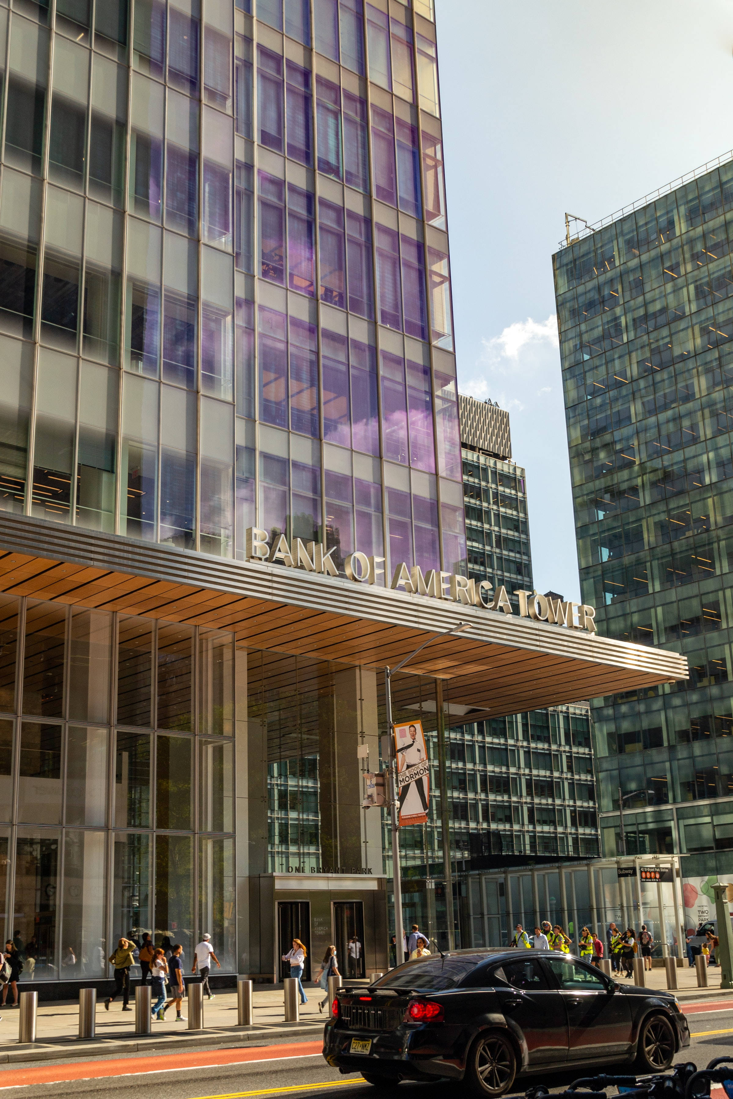 Skyscraper 桌布 壁紙 — 現代玻璃摩天大樓帶有「BANK OF AMERICA TOWER」標誌，聳立於繁忙的城市街道上，有行人和一輛黑色汽車。