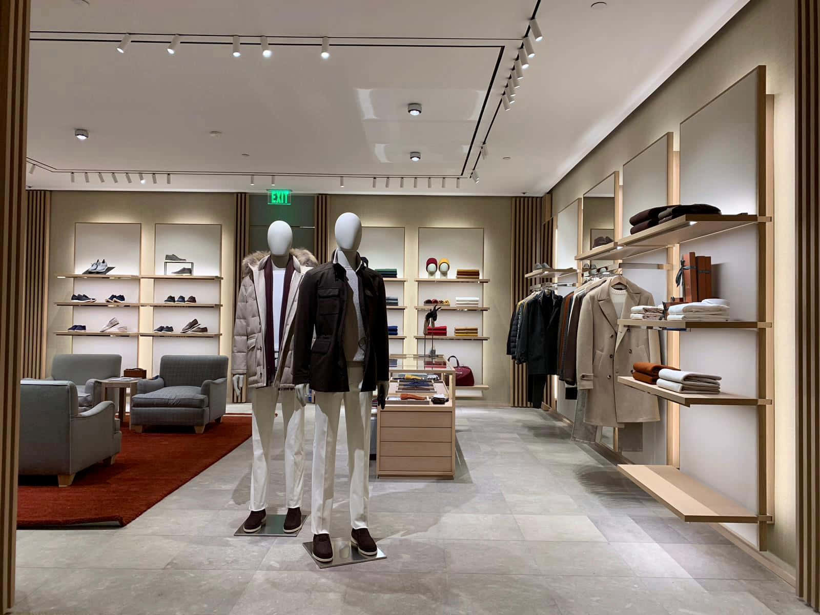 Store 桌布 壁紙 — 現代男士服裝店，人體模型穿著時尚外套，整齊排列的鞋子和配件貨架，在明亮的軌道燈光下。