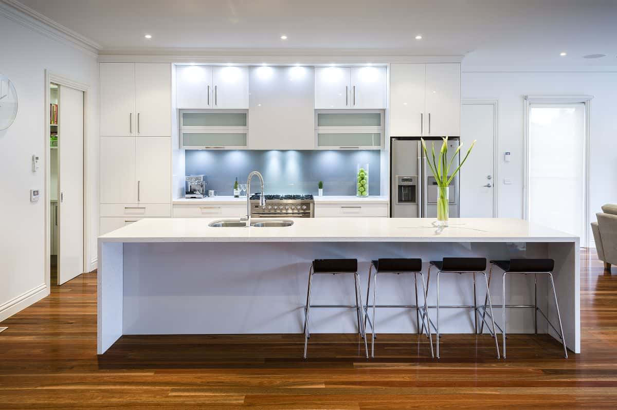 kitchen 桌布 壁紙 — 現代白色廚房，配以時尚中島吧檯椅和溫暖木地板，在明亮嵌入式燈光下。