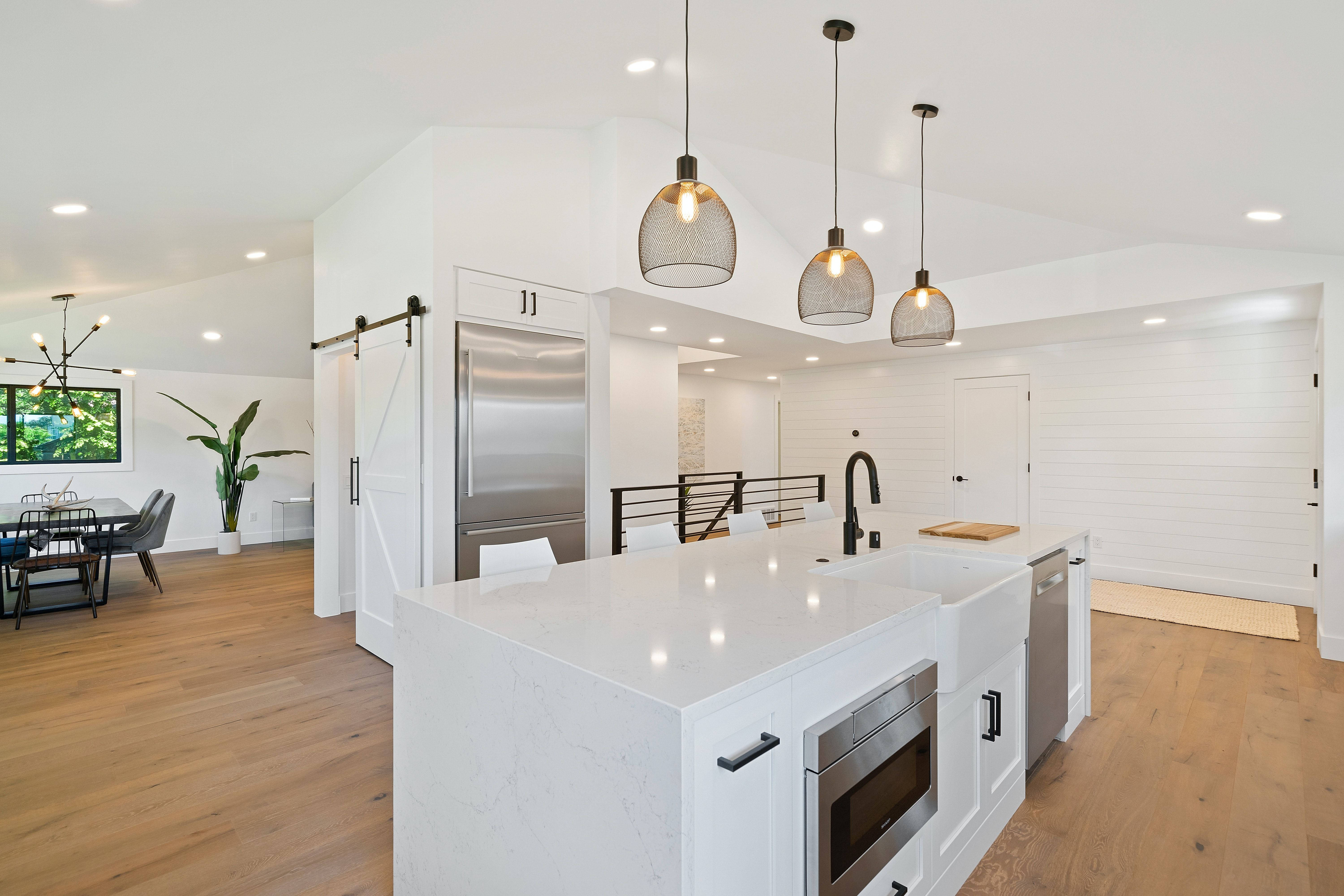 Interior Design 桌布 壁紙 — 現代白色廚房，配有大理石中島、不鏽鋼電器和木地板上方的吊燈。